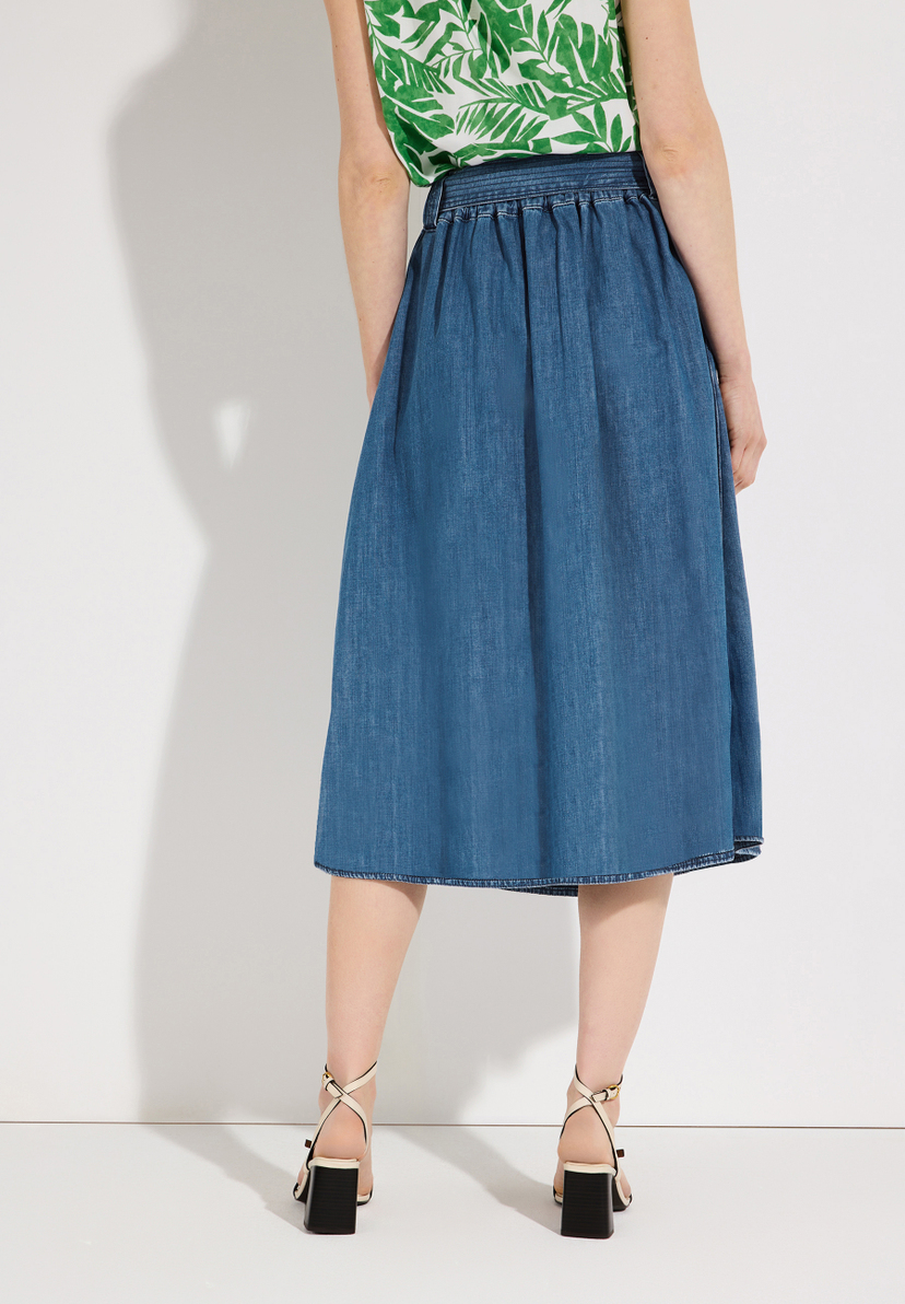 Eine Person trägt einen Jeansrock der Marke MORE & MORE und Sandalen mit Absatz. Eine Person trägt einen Jeansrock der Marke MORE & MORE und Sandalen mit Absatz.