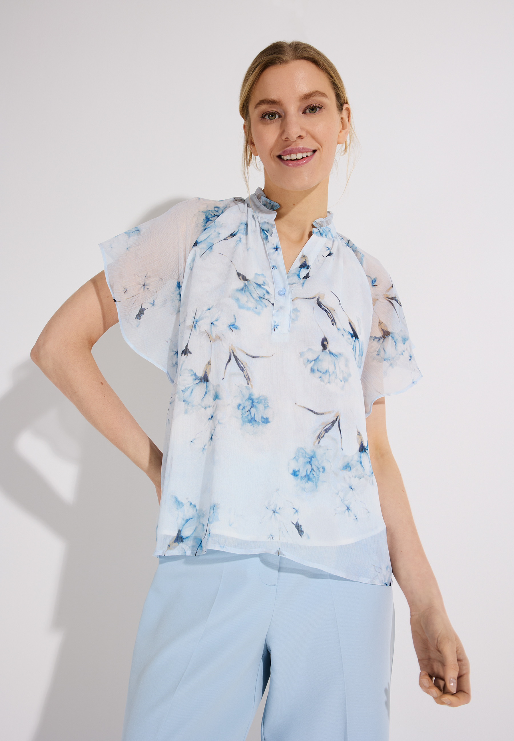 Eine Frau in einer Chiffon-Bluse von MORE & MORE mit blauem Blumenmuster. Eine Frau in einer Chiffon-Bluse von MORE & MORE mit blauem Blumenmuster.