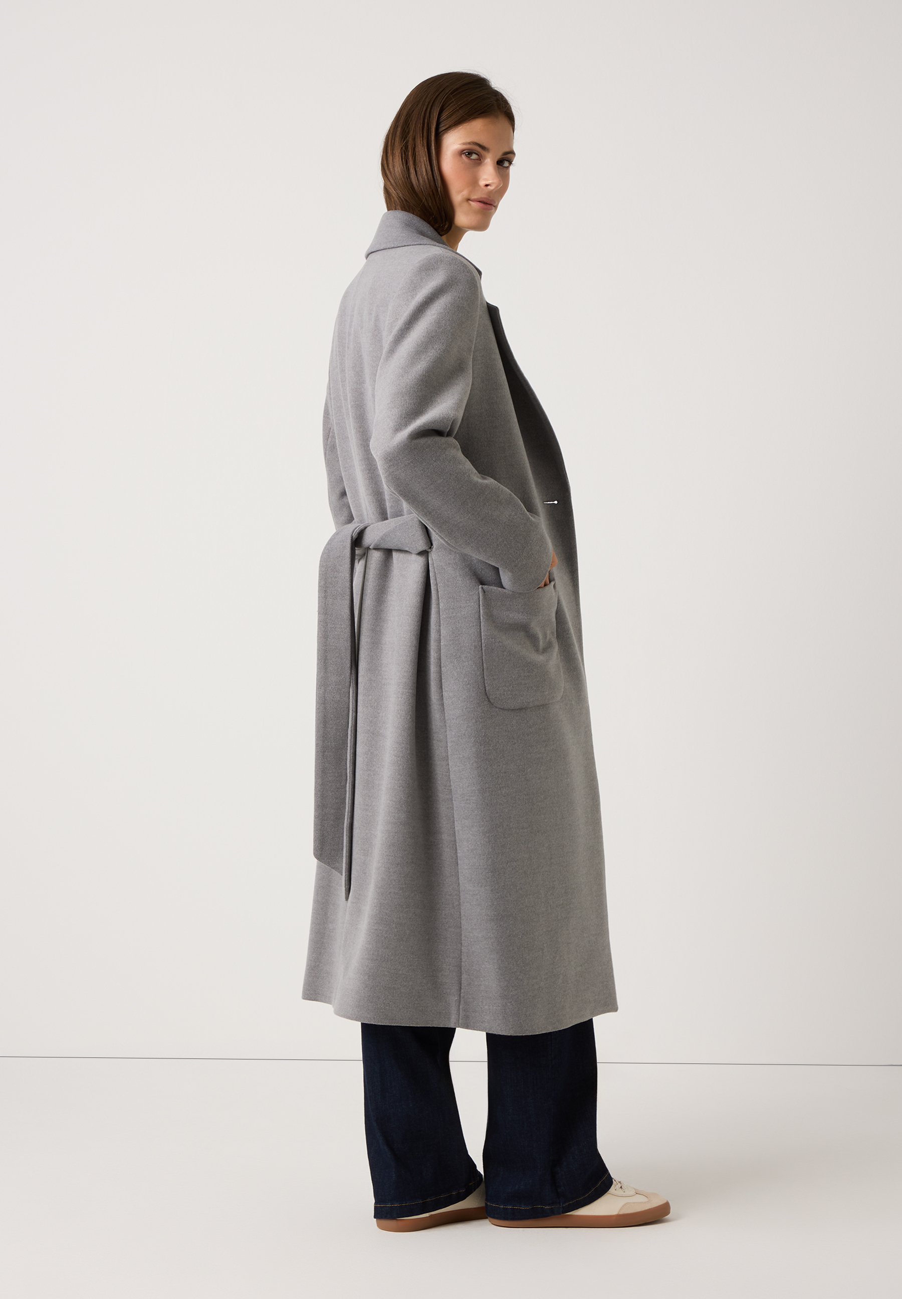 Eine Frau trägt einen grauen MORE & MORE Mantel aus Webware mit Gürtel. Angenehmer Tragekomfort. Eine Frau trägt einen grauen MORE & MORE Mantel aus Webware mit Gürtel. Angenehmer Tragekomfort.