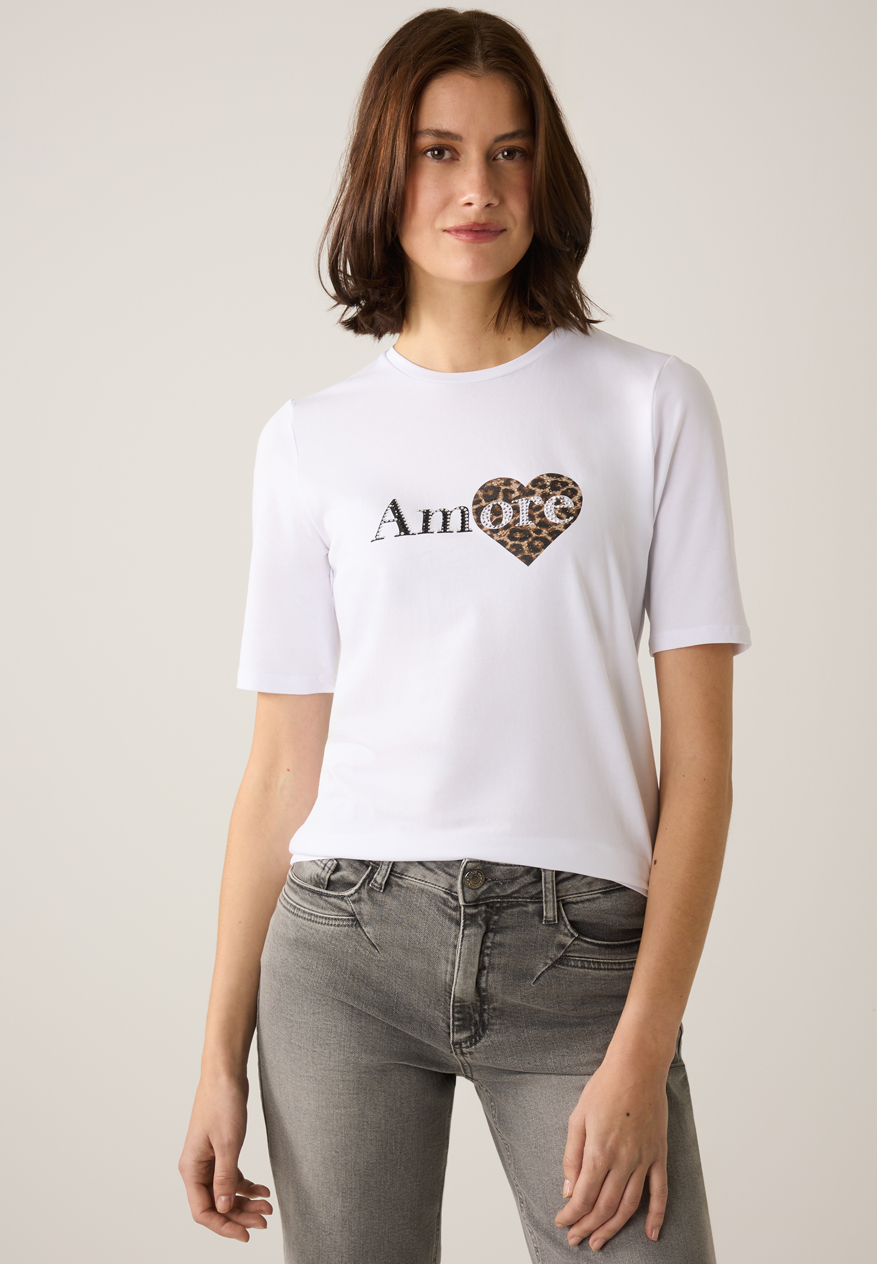 Eine Frau in einem weißen MORE & MORE T-Shirt mit „Amore“-Aufdruck und Leopardenherz.