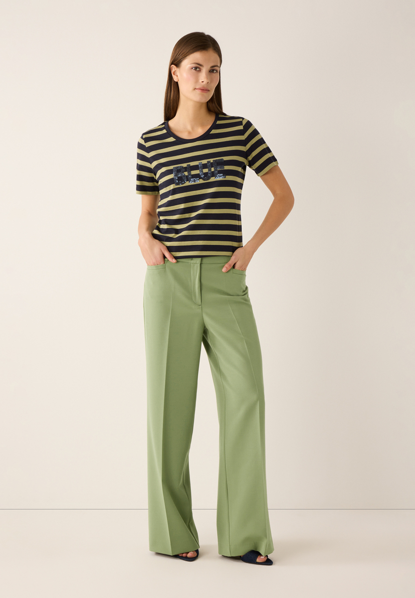 Eine Frau mit MORE & MORE Hose in Olivgrün mit weitem Bein und T-Shirt mit Streifenmuster. Eine Frau mit MORE & MORE Hose in Olivgrün mit weitem Bein und T-Shirt mit Streifenmuster.