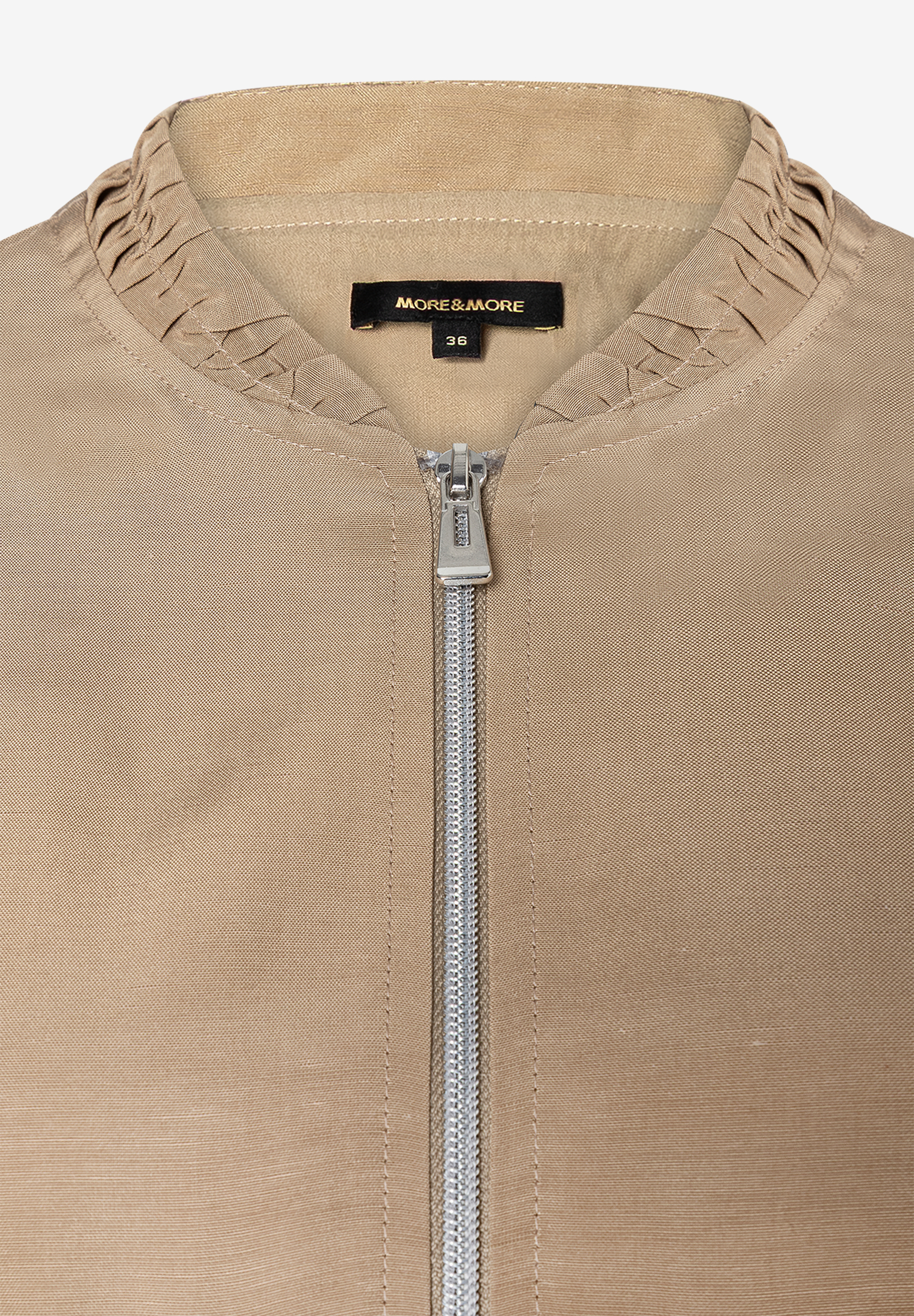 Detailaufnahme einer MORE & MORE Jacke mit Reißverschluss und Markenemblem. Detailaufnahme einer MORE & MORE Jacke mit Reißverschluss und Markenemblem.