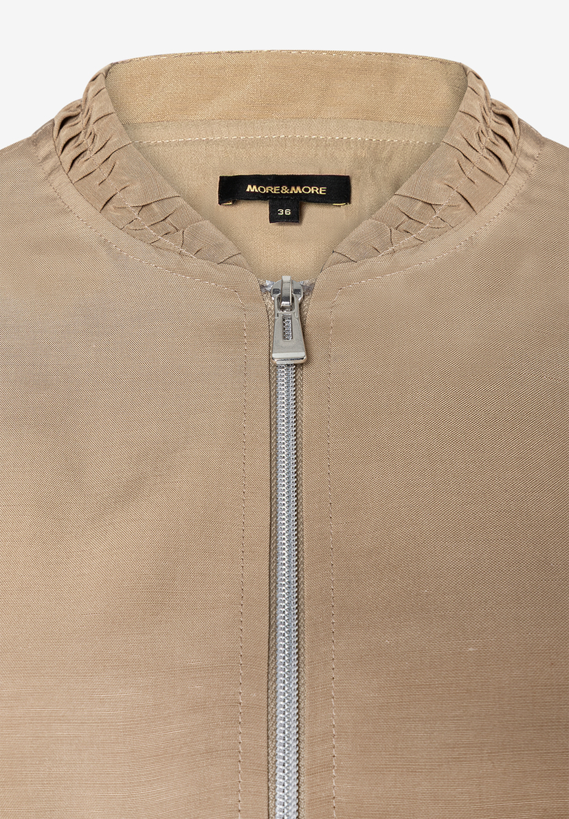Detailaufnahme einer MORE & MORE Jacke mit Reißverschluss und Markenemblem. Detailaufnahme einer MORE & MORE Jacke mit Reißverschluss und Markenemblem.