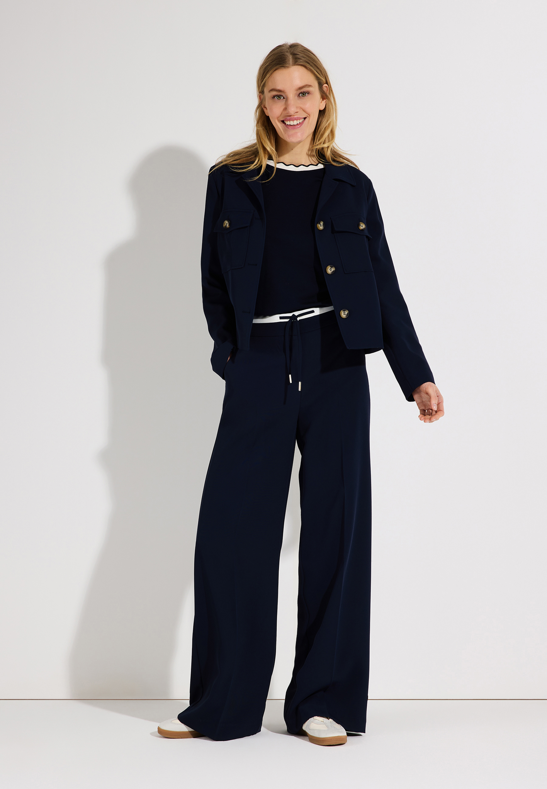 Eine Frau in MORE & MORE Oberteilen und weiten, marineblauen Hosen mit weißem Gürtel. Eine Frau in MORE & MORE Oberteilen und weiten, marineblauen Hosen mit weißem Gürtel.