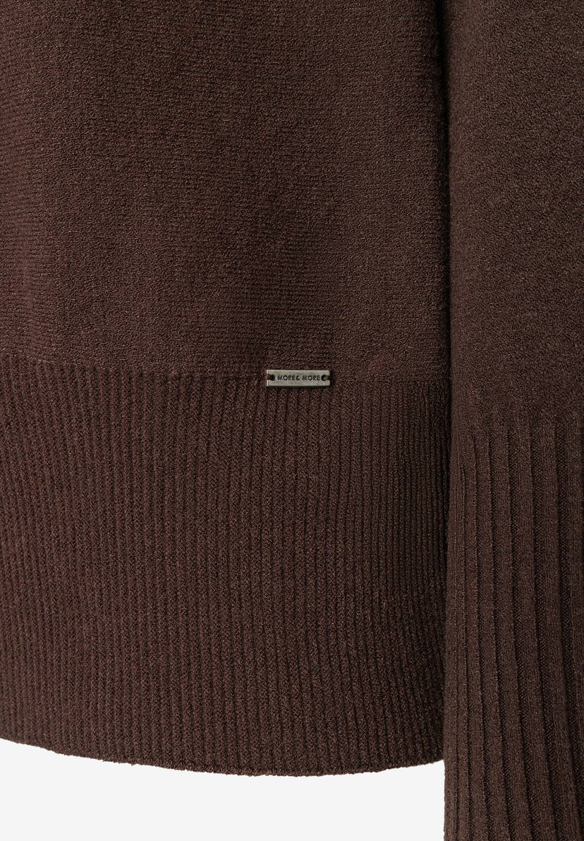 MORE & MORE Pullover & Strickwaren: Nahaufnahme des braunen Pullovers mit Rippstrickbund, kleines silbernes MORE & MORE Logo auf Brusthöhe. MORE & MORE Pullover & Strickwaren: Nahaufnahme des braunen Pullovers mit Rippstrickbund, kleines silbernes MORE & MORE Logo auf Brusthöhe.