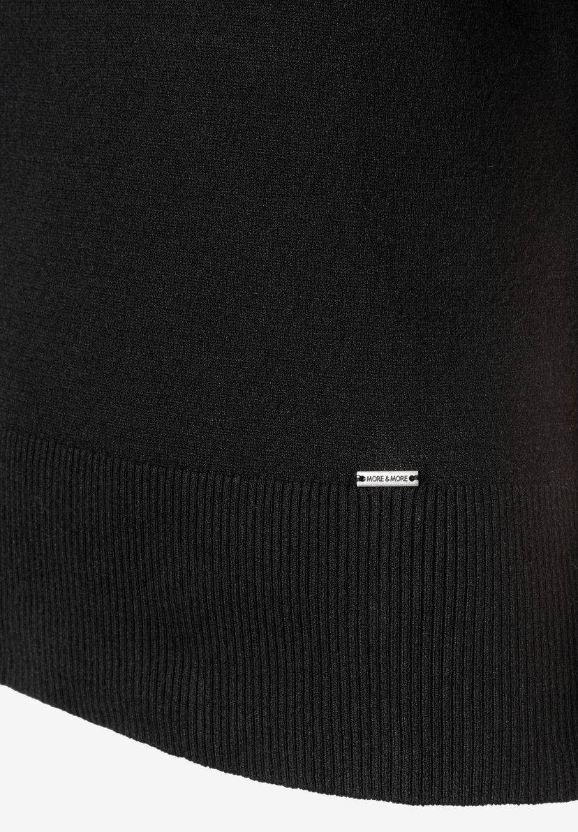 Detailaufnahme eines schwarzen MORE & MORE Feinstrick-Oberteils mit Rippstrick und Logo-Etikett. Detailaufnahme eines schwarzen MORE & MORE Feinstrick-Oberteils mit Rippstrick und Logo-Etikett.