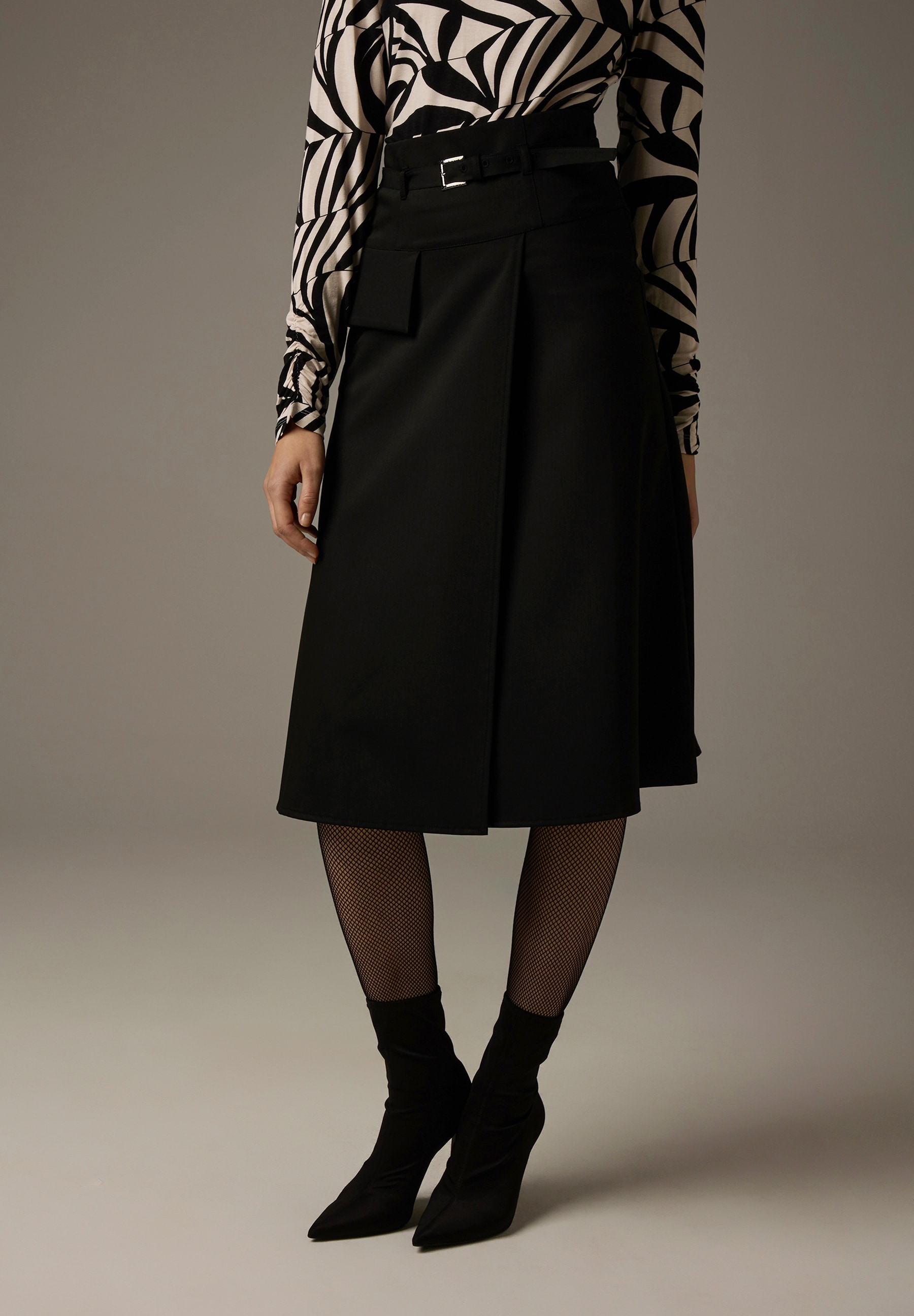 Ein Rock von MORE & MORE in Schwarz mit einem Print-Oberteil und schwarzen Stiefeletten. Ein Rock von MORE & MORE in Schwarz mit einem Print-Oberteil und schwarzen Stiefeletten.