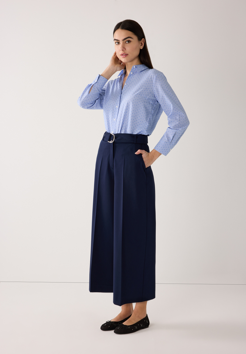 Eine Frau posiert in einer blauen MORE & MORE Bluse und einer fließenden, marineblauen Webware-Hose mit Gürtel. Eine Frau posiert in einer blauen MORE & MORE Bluse und einer fließenden, marineblauen Webware-Hose mit Gürtel.