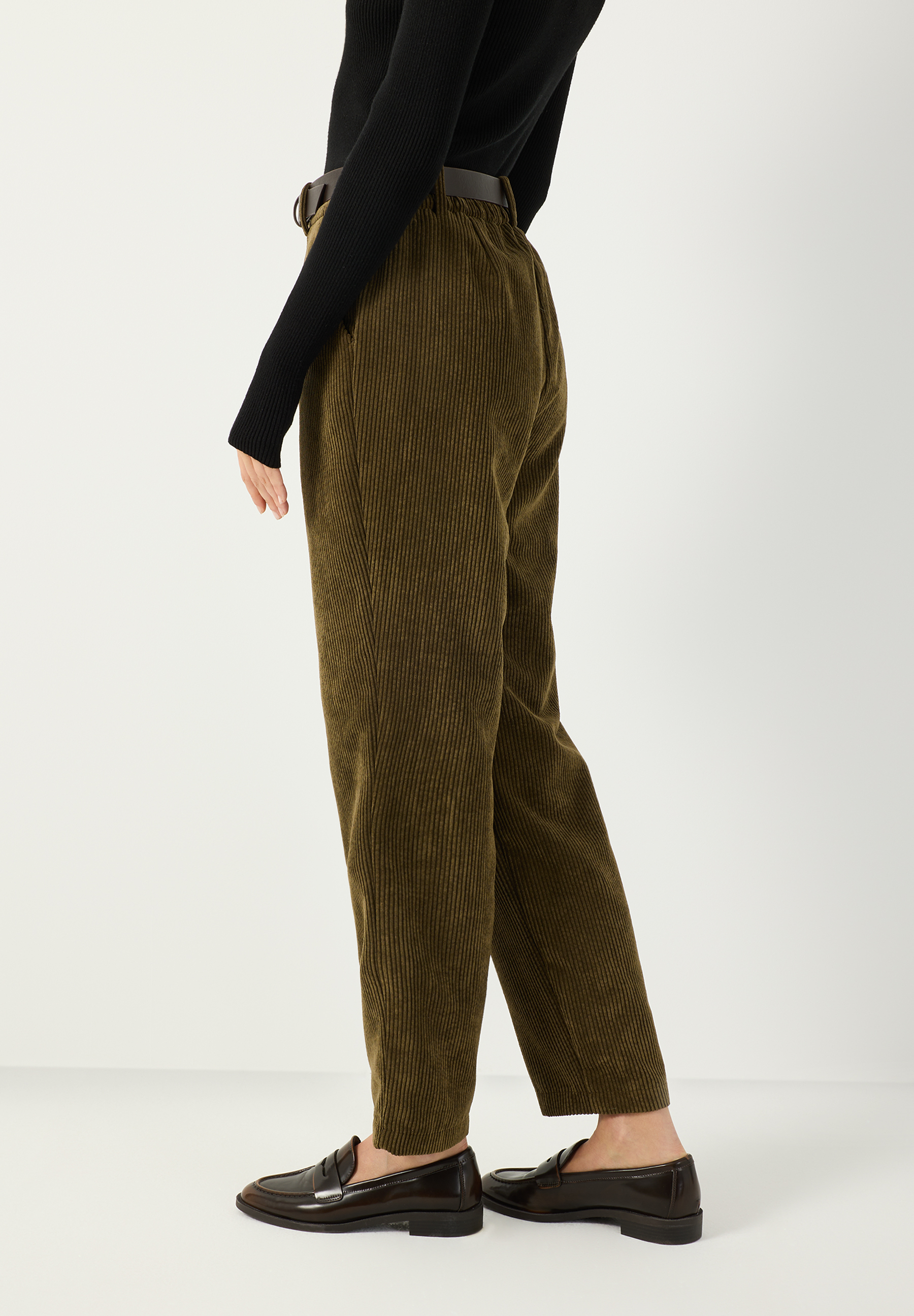 MORE & MORE Cordhose in Olivgrün mit schwarzem Rollkragenpullover und braunen Slippern, seitliche Ansicht.