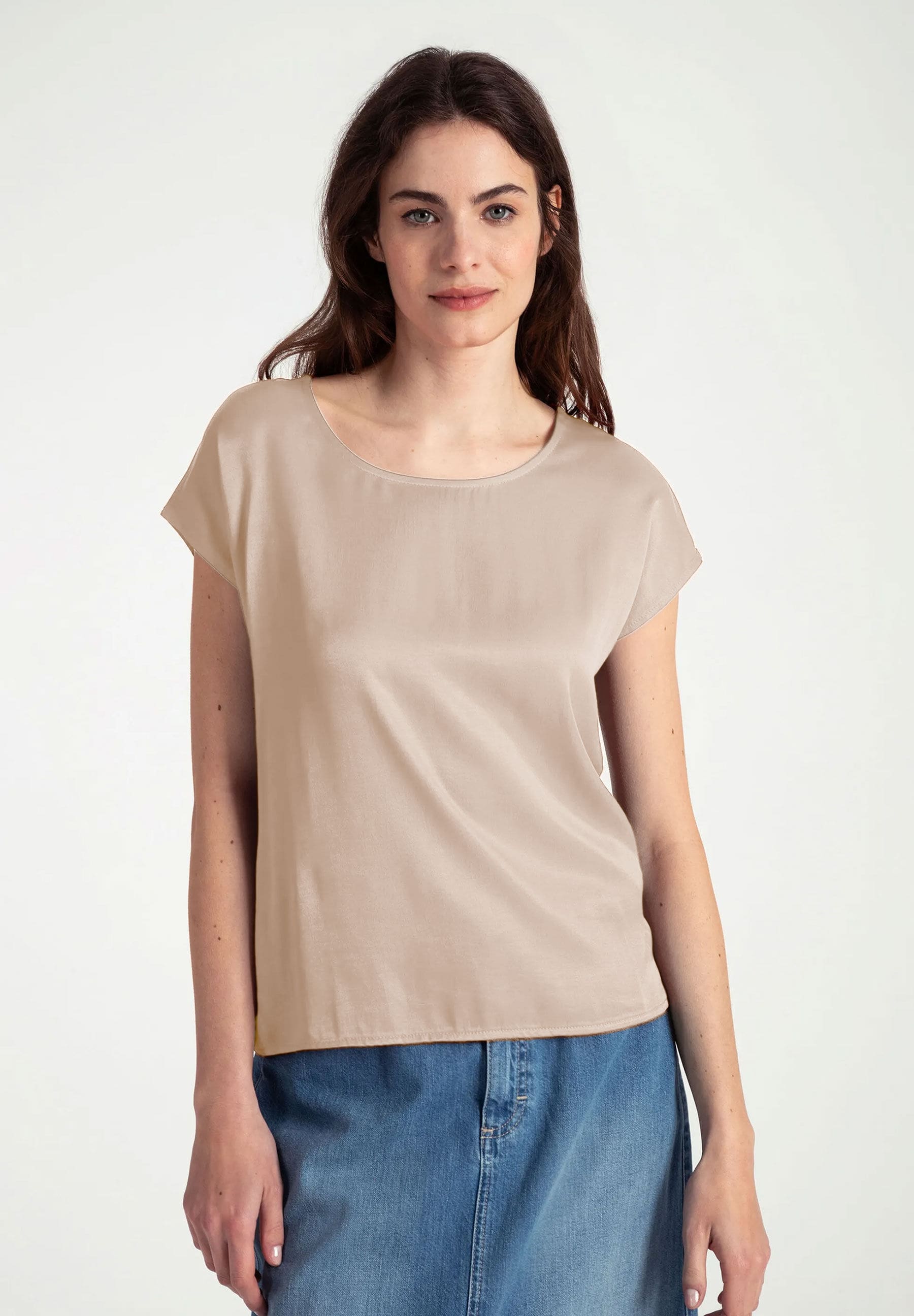 Eine Frau trägt ein MORE & MORE-Top aus Materialmix mit seidigem Glanz und Jersey, kombiniert mit einem Jeansrock.
