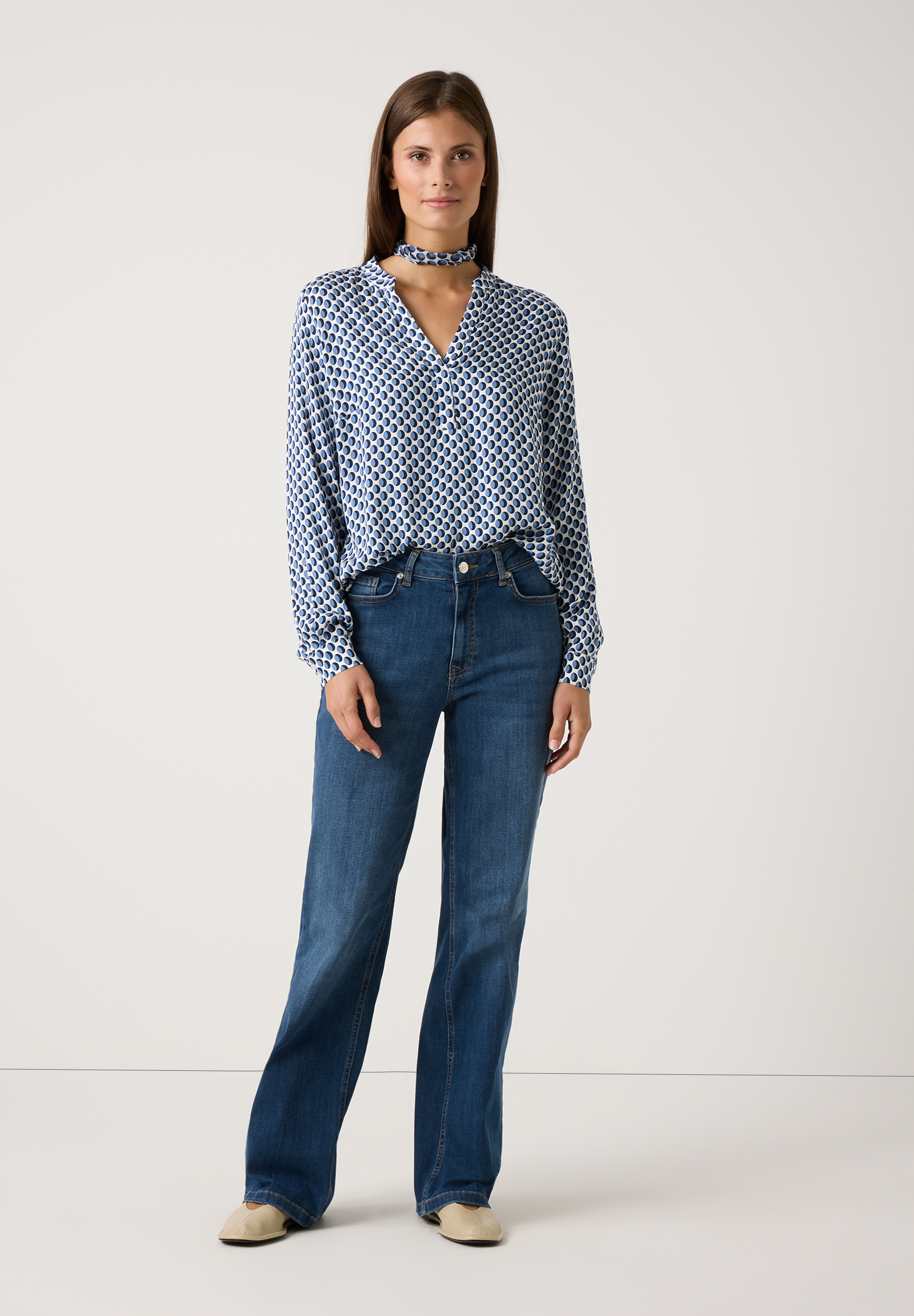Eine Frau trägt eine blaue Viskosebluse von MORE & MORE mit Muster und Jeans vor einem weißen Hintergrund. Eine Frau trägt eine blaue Viskosebluse von MORE & MORE mit Muster und Jeans vor einem weißen Hintergrund.