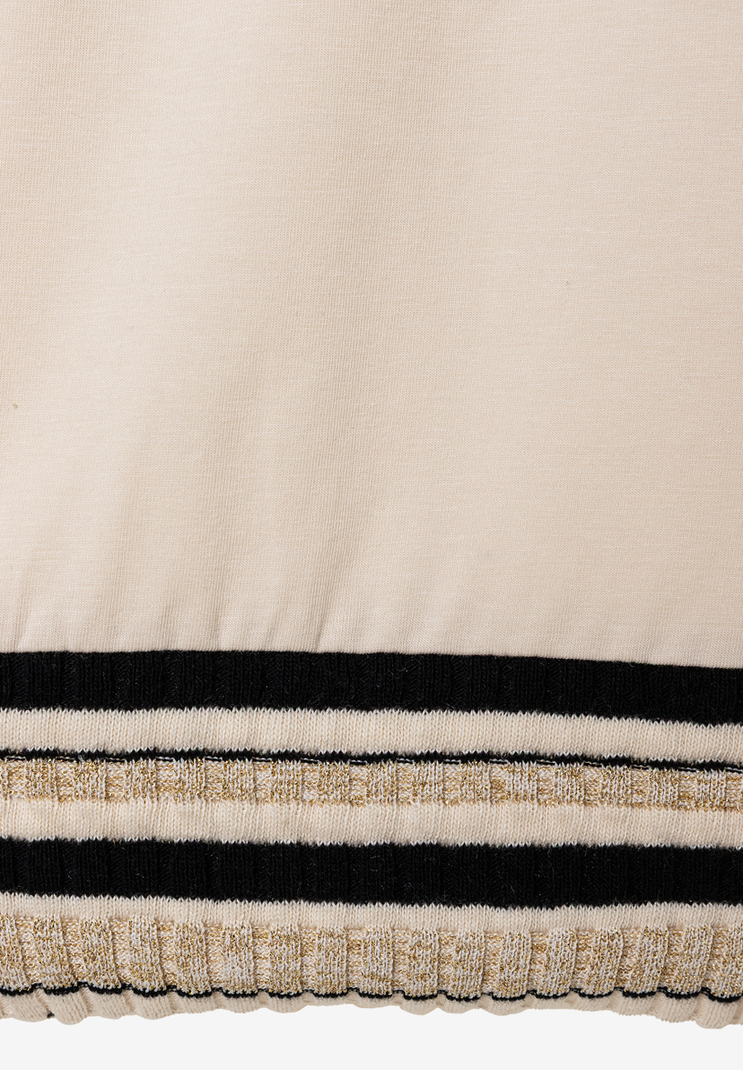 Nahaufnahme eines MORE & MORE Oberteils mit Jersey-Material. Es hat schwarzen, weißen und goldenen Streifen am unteren Rand. Nahaufnahme eines MORE & MORE Oberteils mit Jersey-Material. Es hat schwarzen, weißen und goldenen Streifen am unteren Rand.