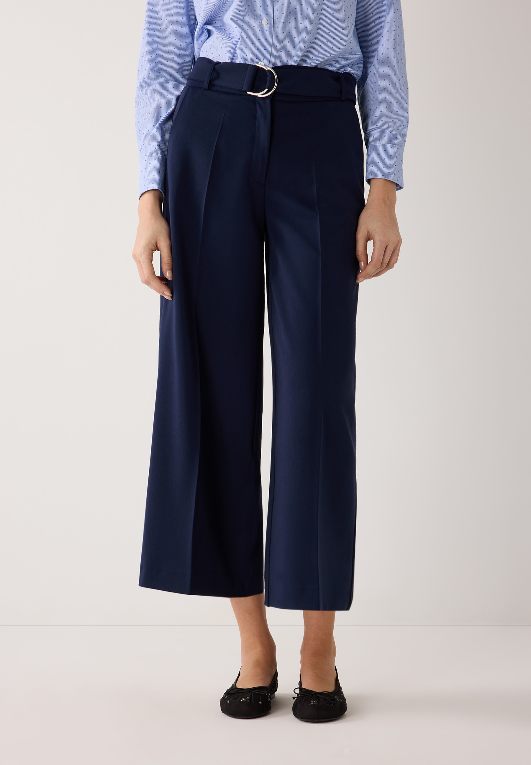 Eine Person trägt eine blaue MORE & MORE Hose. Die fließende Hose hat einen Gürtel mit silberner Schnalle. Eine Person trägt eine blaue MORE & MORE Hose. Die fließende Hose hat einen Gürtel mit silberner Schnalle.