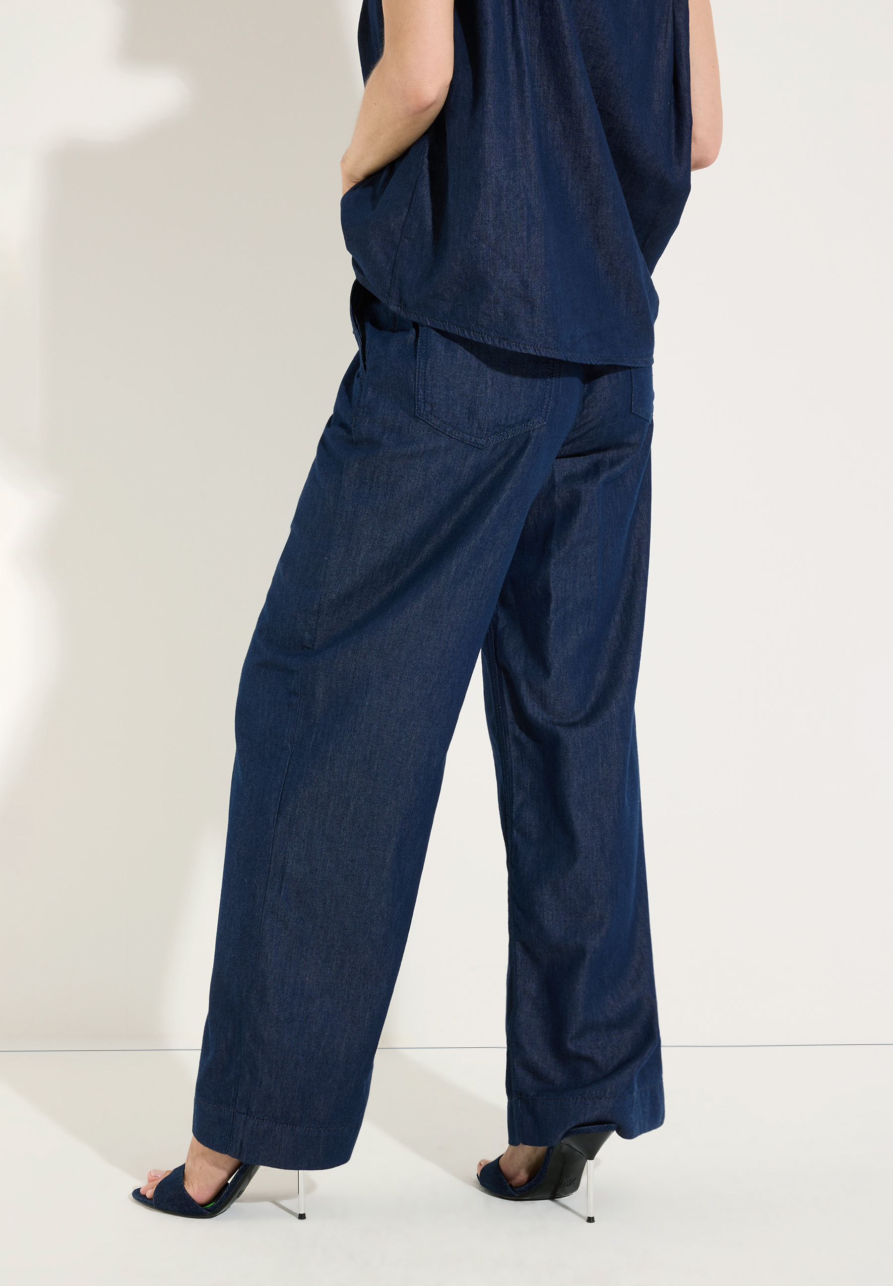MORE & MORE Jeans: Rückansicht einer Frau in dunkelblauer Denim-Hose mit weitem Bein und passendem Oberteil, elegant gestylt. MORE & MORE Jeans: Rückansicht einer Frau in dunkelblauer Denim-Hose mit weitem Bein und passendem Oberteil, elegant gestylt.