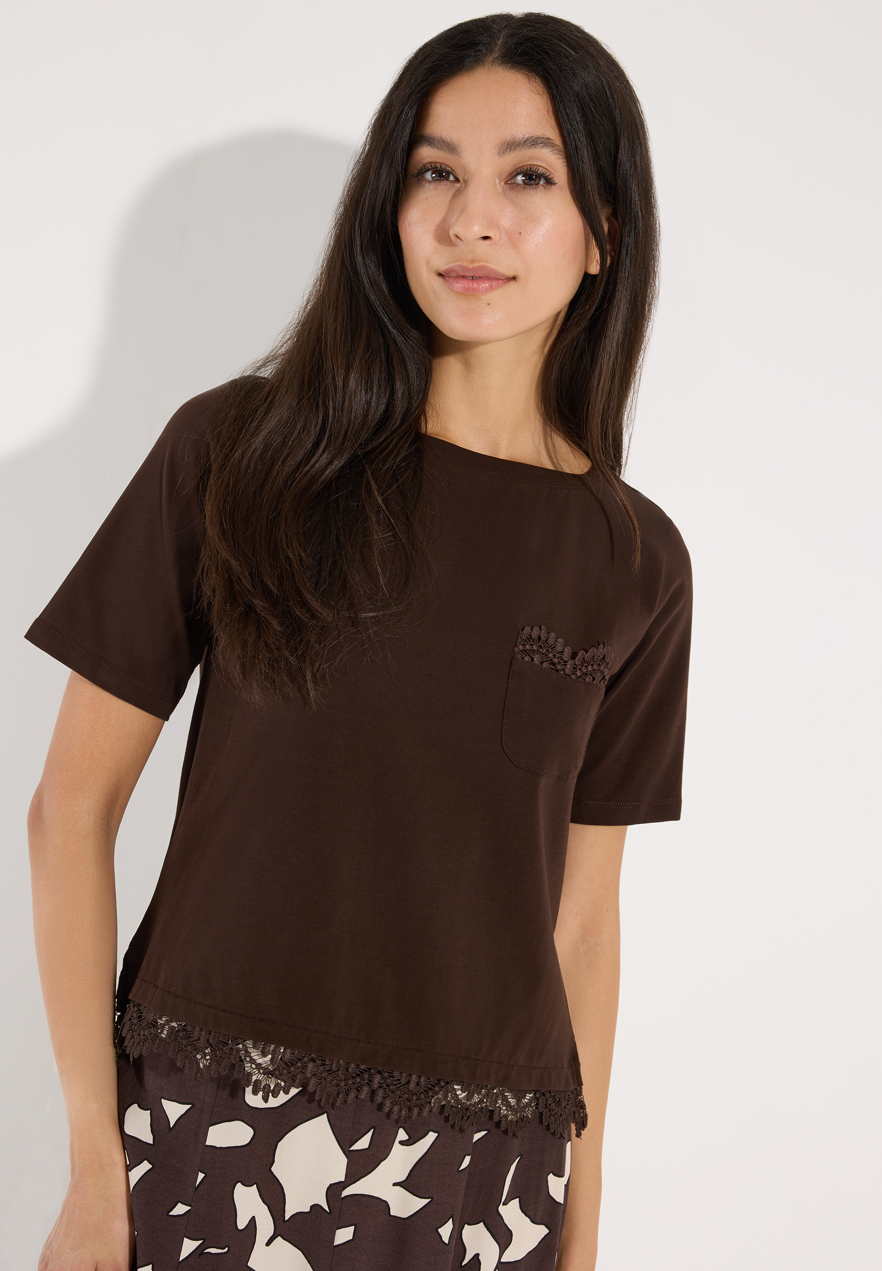 MORE & MORE T-Shirt in Braun, das eine junge Frau zeigt. Es hat kurze Ärmel, einen runden Halsausschnitt und eine verzierte Tasche.