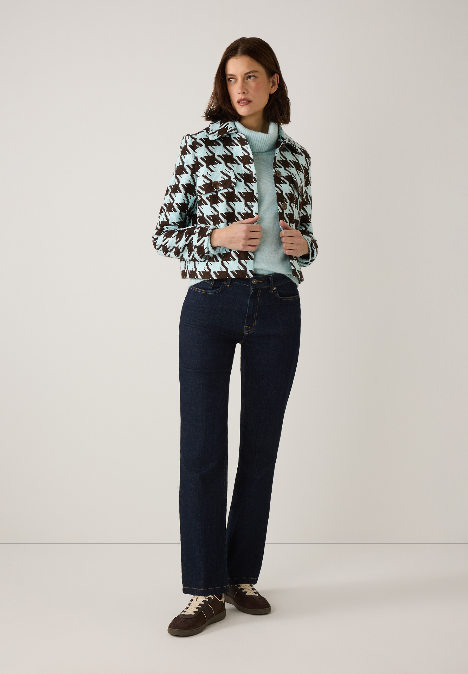 Eine Frau trägt MORE & MORE Strick-Oberteile mit Hahnentrittmuster, kombiniert mit Jeans und Schuhen. Eine Frau trägt MORE & MORE Strick-Oberteile mit Hahnentrittmuster, kombiniert mit Jeans und Schuhen.