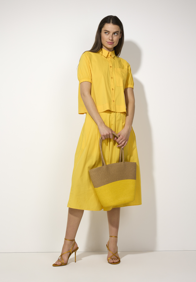Eine Frau in gelber MORE & MORE Bluse und Rock, hält eine Tasche in Gelb und Braun. Eine Frau in gelber MORE & MORE Bluse und Rock, hält eine Tasche in Gelb und Braun.