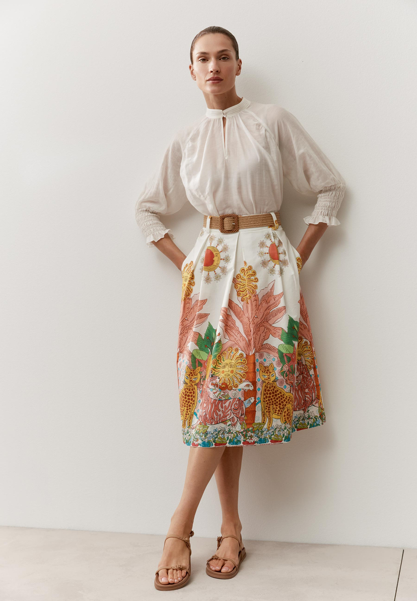 Eine Frau in MORE & MORE Bluse und Rock mit Dschungelmotiven posiert vor einer weißen Wand. Eine Frau in MORE & MORE Bluse und Rock mit Dschungelmotiven posiert vor einer weißen Wand.