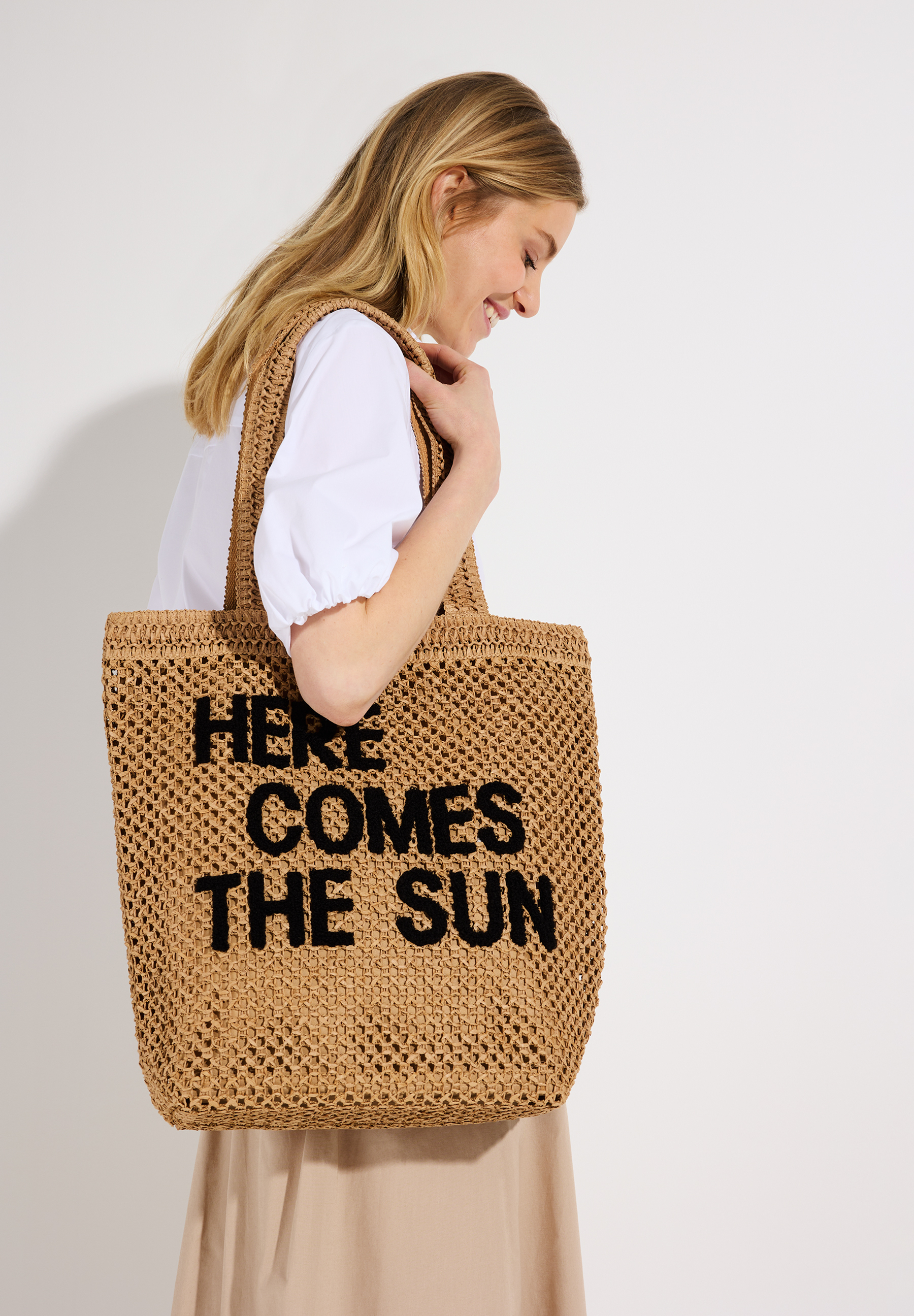 Eine Frau mit einer MORE & MORE Tasche. Auf der Tasche steht: "HERE COMES THE SUN".