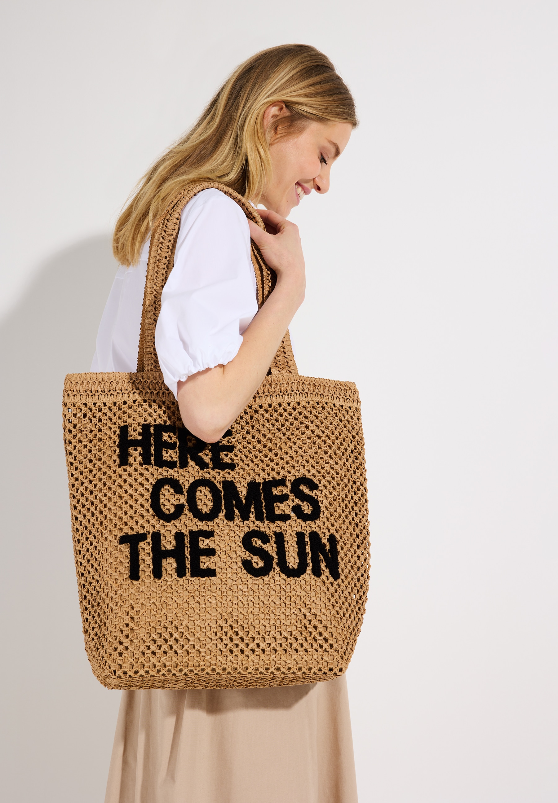 Eine Frau mit einer MORE & MORE Tasche. Auf der Tasche steht: "HERE COMES THE SUN". Eine Frau mit einer MORE & MORE Tasche. Auf der Tasche steht: "HERE COMES THE SUN".