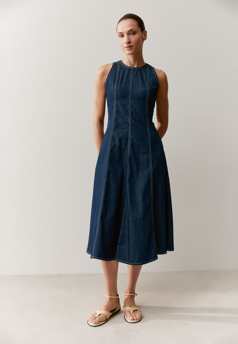 Eine Frau in einem ärmellosen Jeanskleid von MORE & MORE mit A-Linien-Schnitt und weißen Ziernähten.