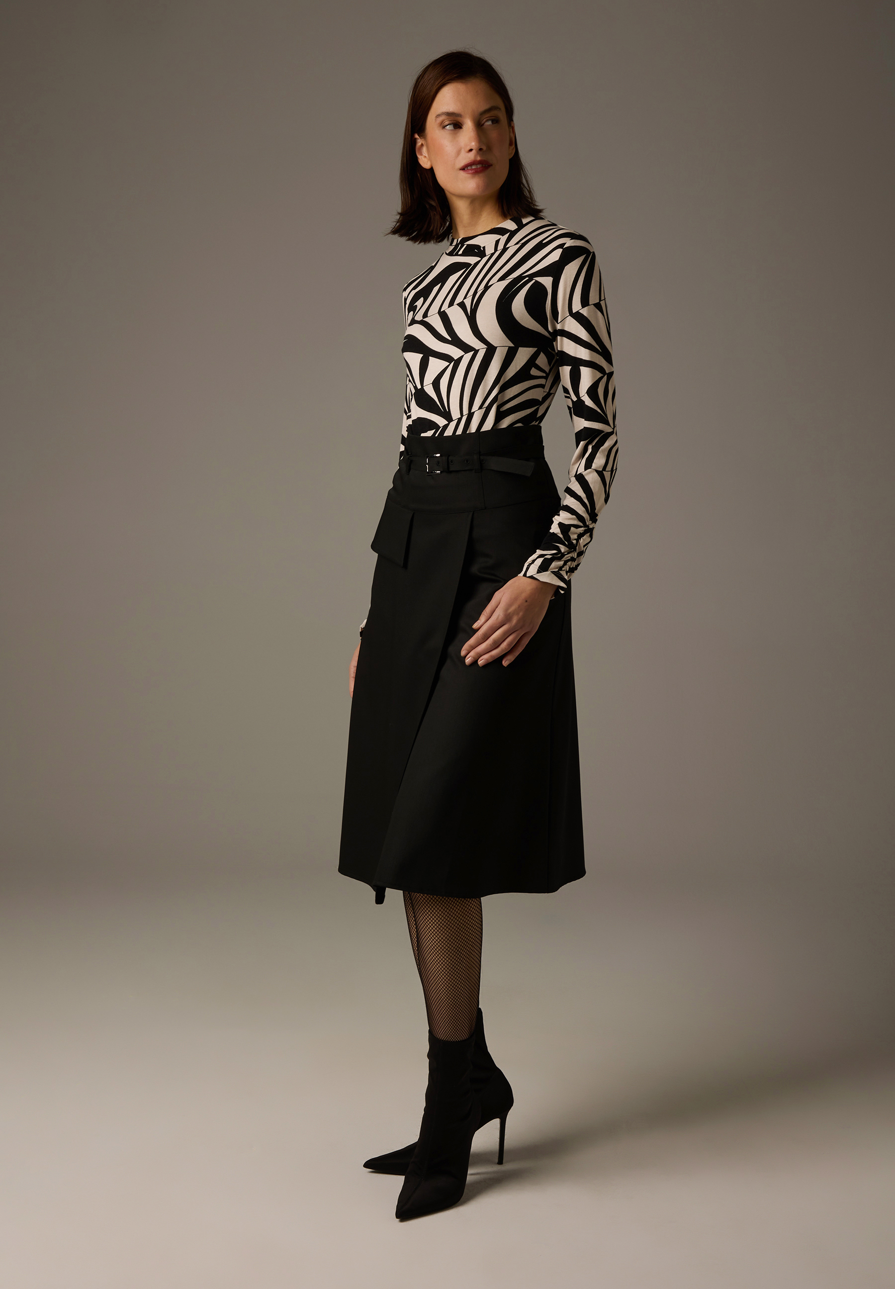 Eine Frau in einem MORE & MORE Oberteil mit Zebra-Print, einem schwarzen Rock und Stiefeln. Eine Frau in einem MORE & MORE Oberteil mit Zebra-Print, einem schwarzen Rock und Stiefeln.