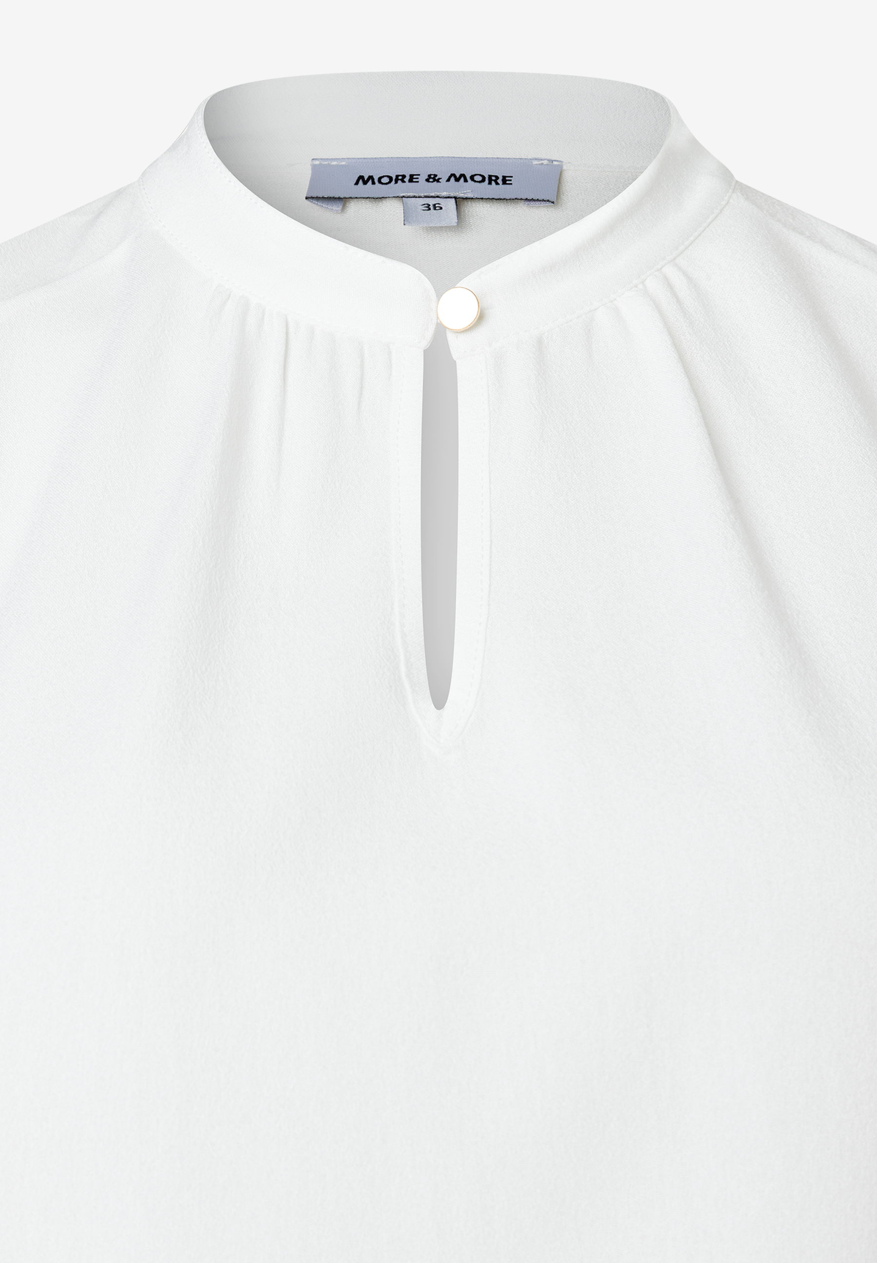 Nahaufnahme einer weißen MORE & MORE Bluse mit Stehkragen und Knopfdetail. Nahaufnahme einer weißen MORE & MORE Bluse mit Stehkragen und Knopfdetail.