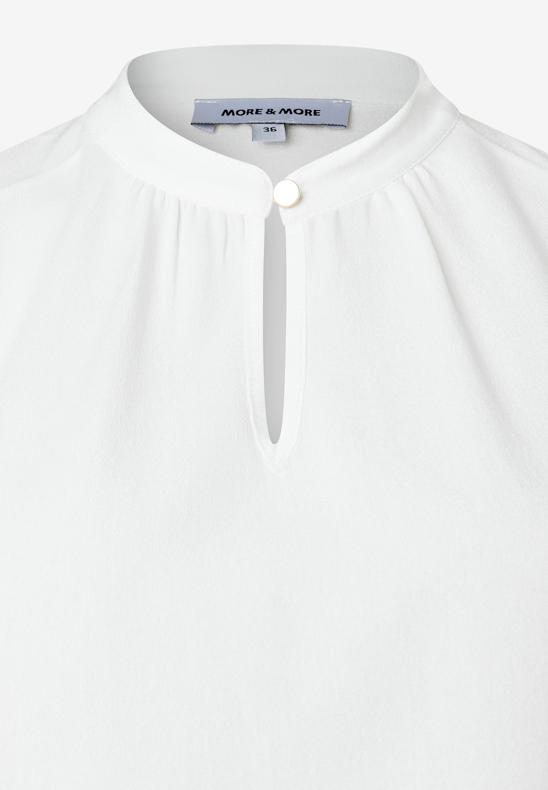 Nahaufnahme einer weißen MORE & MORE Bluse mit Stehkragen und Knopfdetail. Nahaufnahme einer weißen MORE & MORE Bluse mit Stehkragen und Knopfdetail.