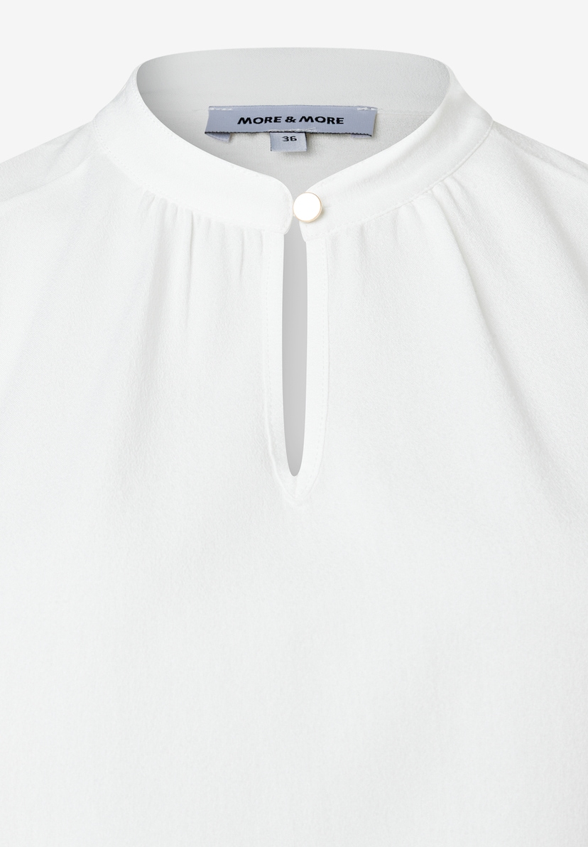 Nahaufnahme einer weißen MORE & MORE Bluse mit Stehkragen und Knopfdetail. Nahaufnahme einer weißen MORE & MORE Bluse mit Stehkragen und Knopfdetail.