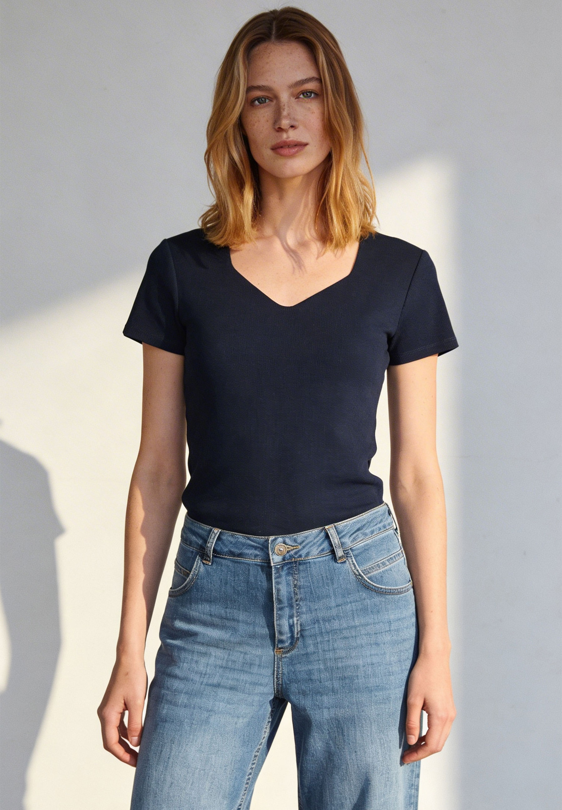 Eine Frau trägt ein geripptes, blaues MORE & MORE Top mit V-Ausschnitt und Jeans.