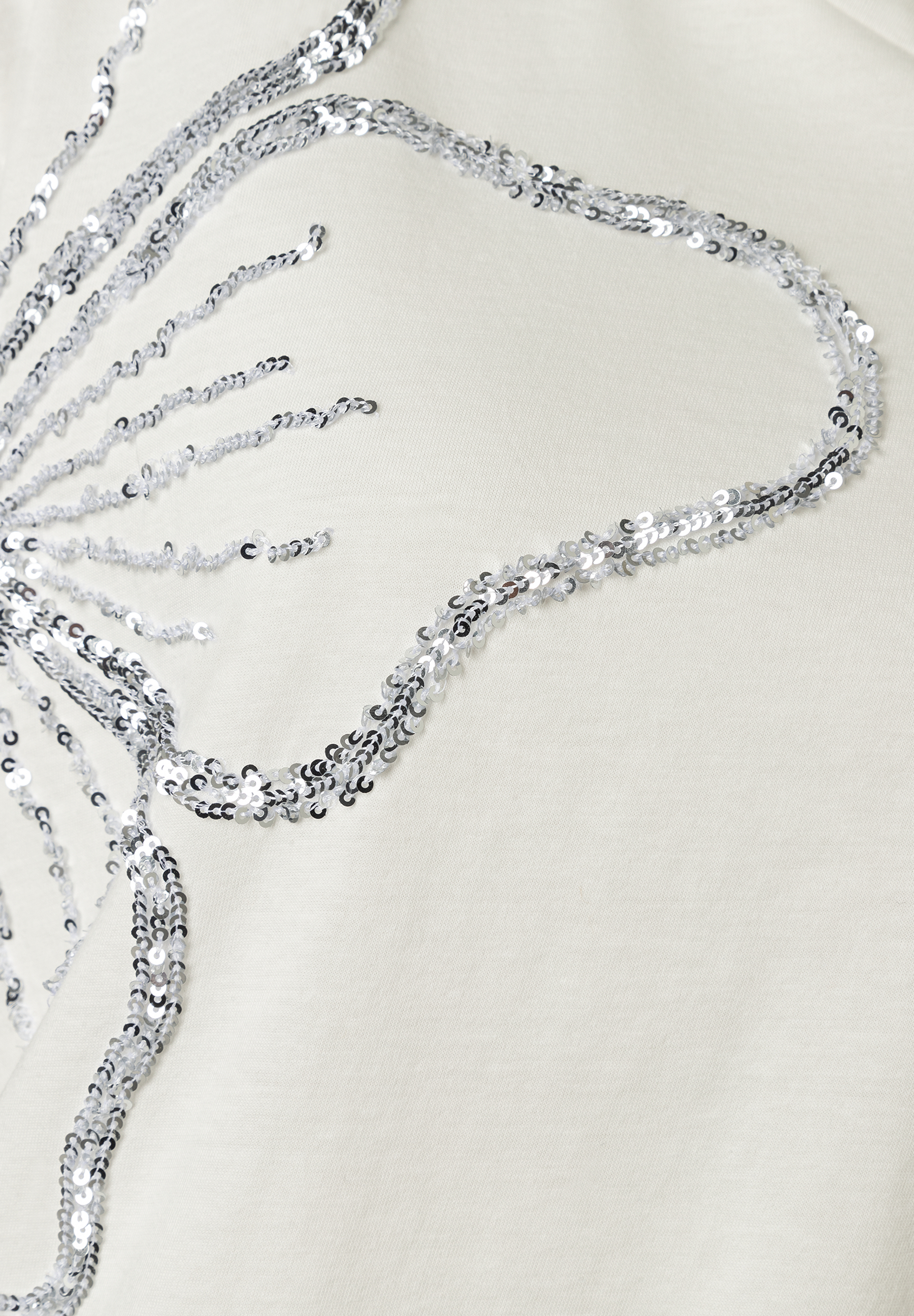 Detailaufnahme eines MORE & MORE Oberteils mit Jersey-Material und silberfarbenem Pailletten-Design. Detailaufnahme eines MORE & MORE Oberteils mit Jersey-Material und silberfarbenem Pailletten-Design.