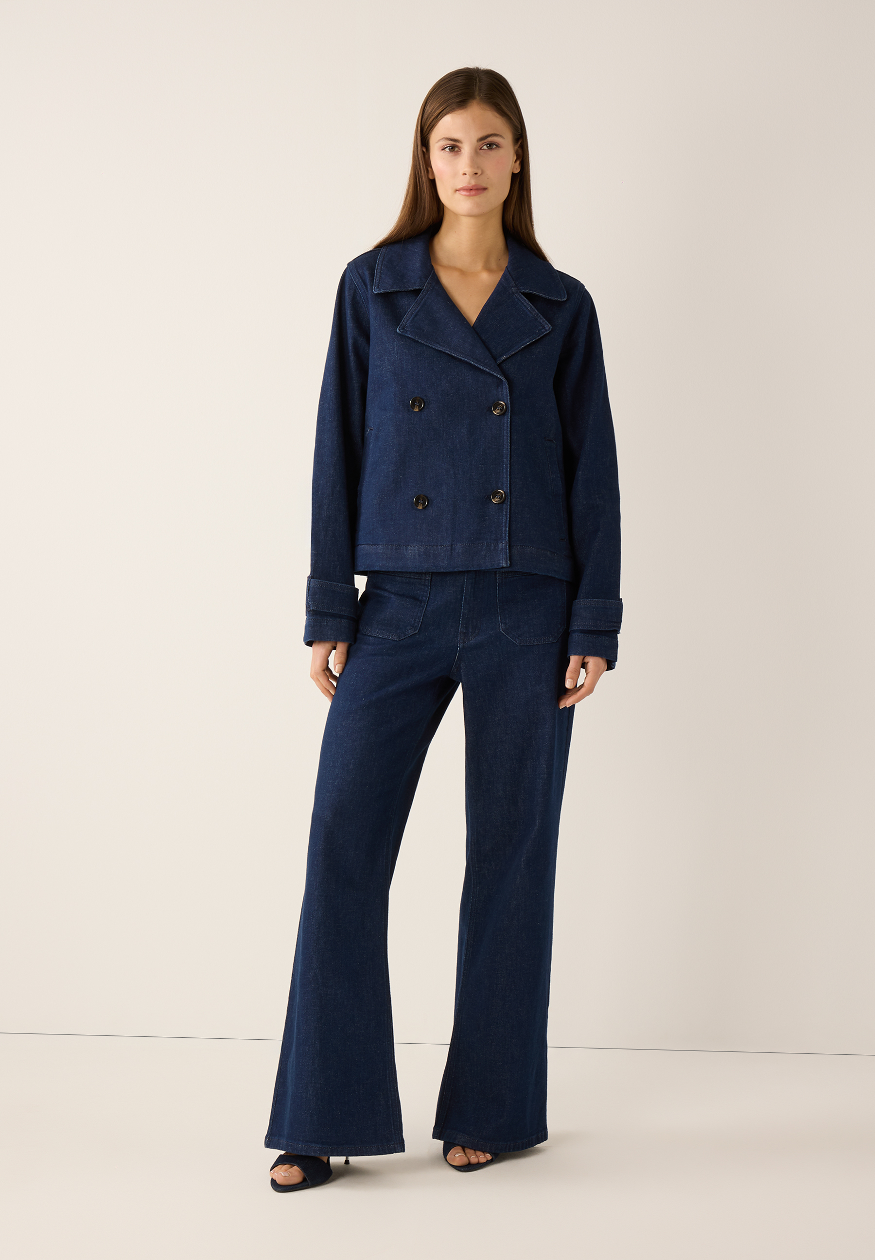 Eine Frau trägt ein Jeans-Ensemble von MORE & MORE, bestehend aus einer Jacke und Schlaghosen. Eine Frau trägt ein Jeans-Ensemble von MORE & MORE, bestehend aus einer Jacke und Schlaghosen.