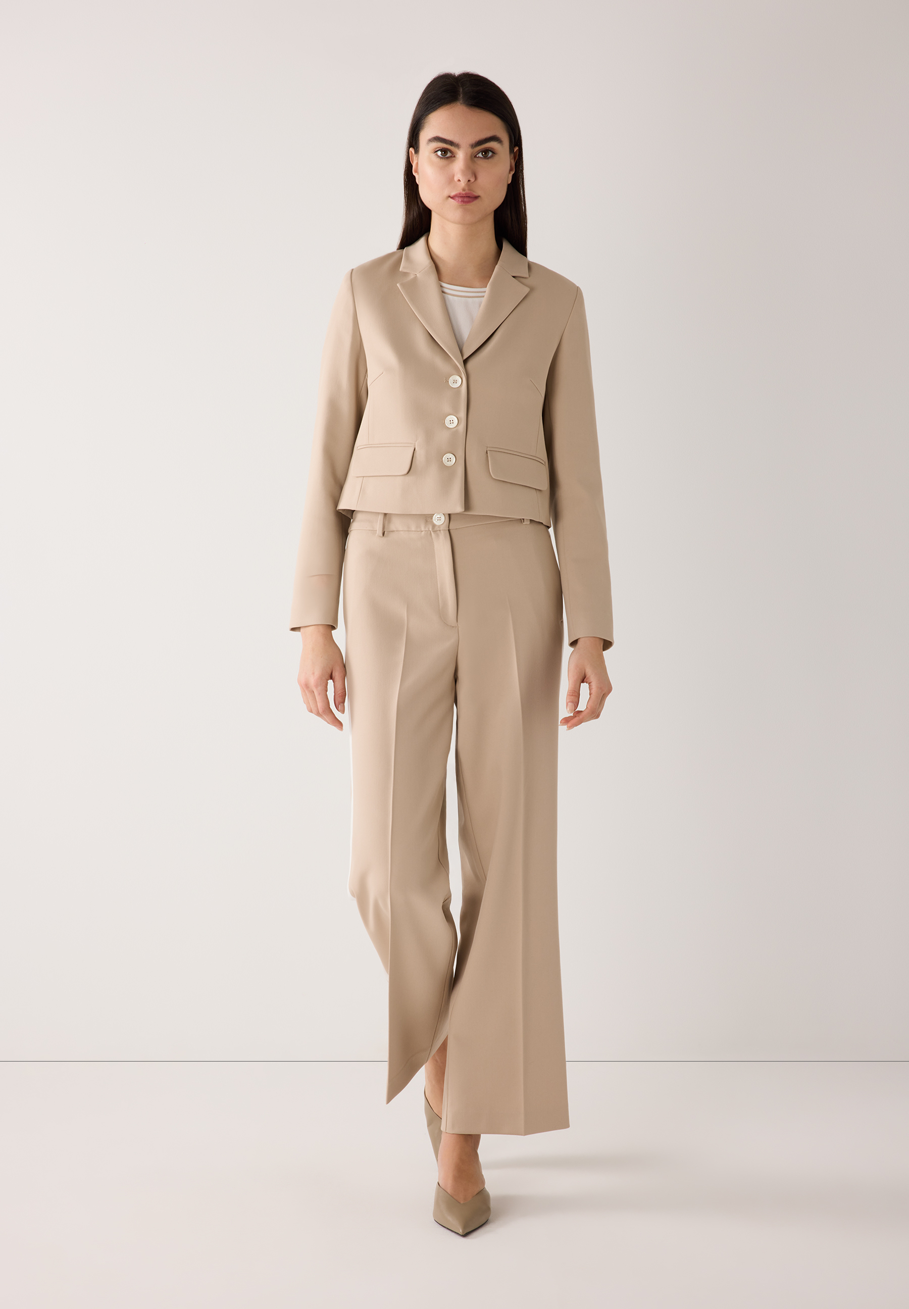 Eine Frau in einem beigen Hosenanzug von MORE & MORE. Die Webware-Hose ist fließend mit hohem Tragekomfort. Eine Frau in einem beigen Hosenanzug von MORE & MORE. Die Webware-Hose ist fließend mit hohem Tragekomfort.