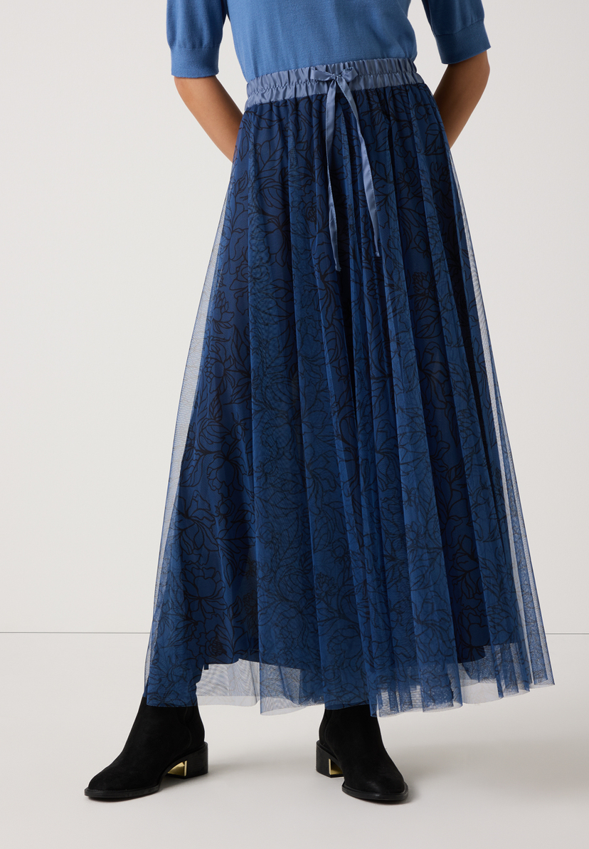 Eine Frau trägt einen langen, blauen MORE & MORE Rock aus Mesh mit schwarzem Blumenmuster. Der Rock hat einen angenehmen, elastischen Bund. Eine Frau trägt einen langen, blauen MORE & MORE Rock aus Mesh mit schwarzem Blumenmuster. Der Rock hat einen angenehmen, elastischen Bund.