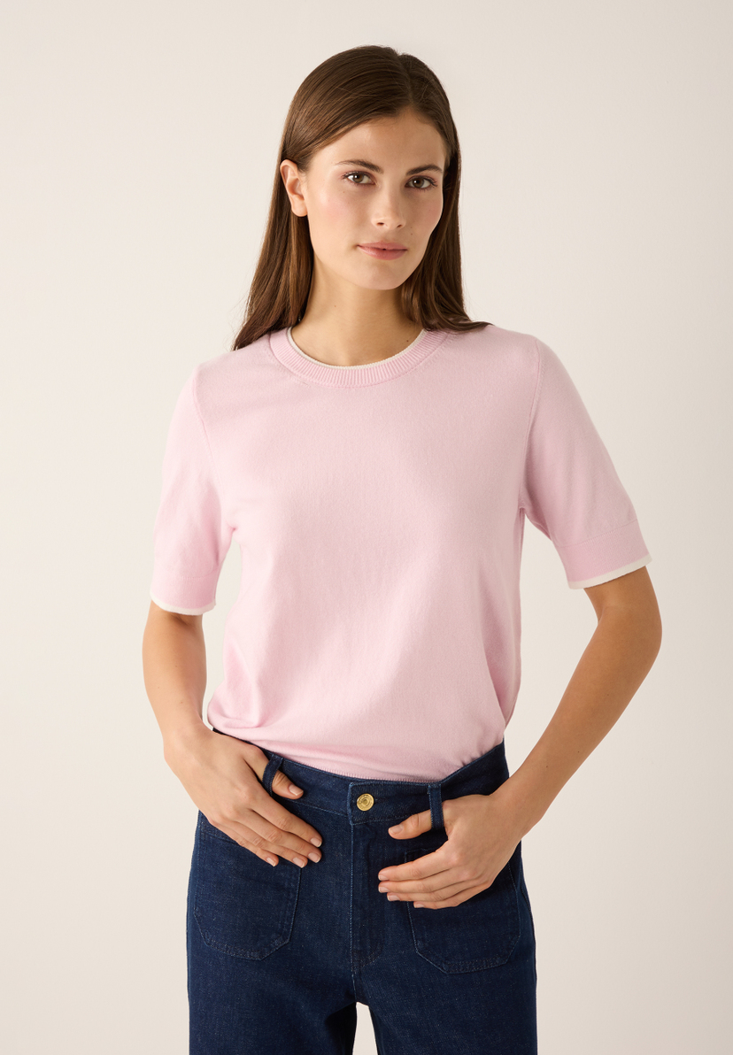 Eine Frau mit MORE & MORE Feinstrick-Oberteil. Der Pullover in Rosa hat kurze Ärmel mit weißen Kanten. Eine Frau mit MORE & MORE Feinstrick-Oberteil. Der Pullover in Rosa hat kurze Ärmel mit weißen Kanten.