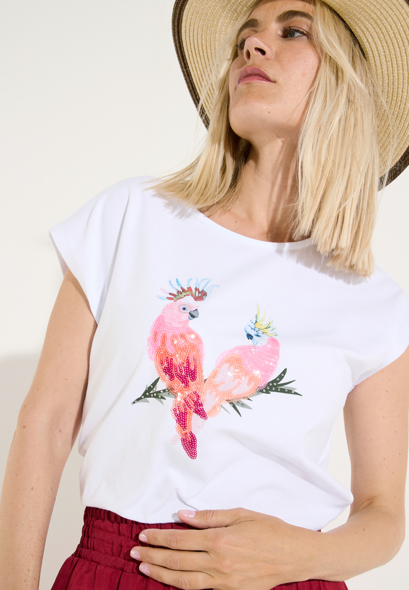 MORE & MORE T-Shirt/Top. Frau mit Hut trägt weißes Shirt mit zwei glitzernden Kakadus, die auf einem Zweig sitzen. MORE & MORE T-Shirt/Top. Frau mit Hut trägt weißes Shirt mit zwei glitzernden Kakadus, die auf einem Zweig sitzen.