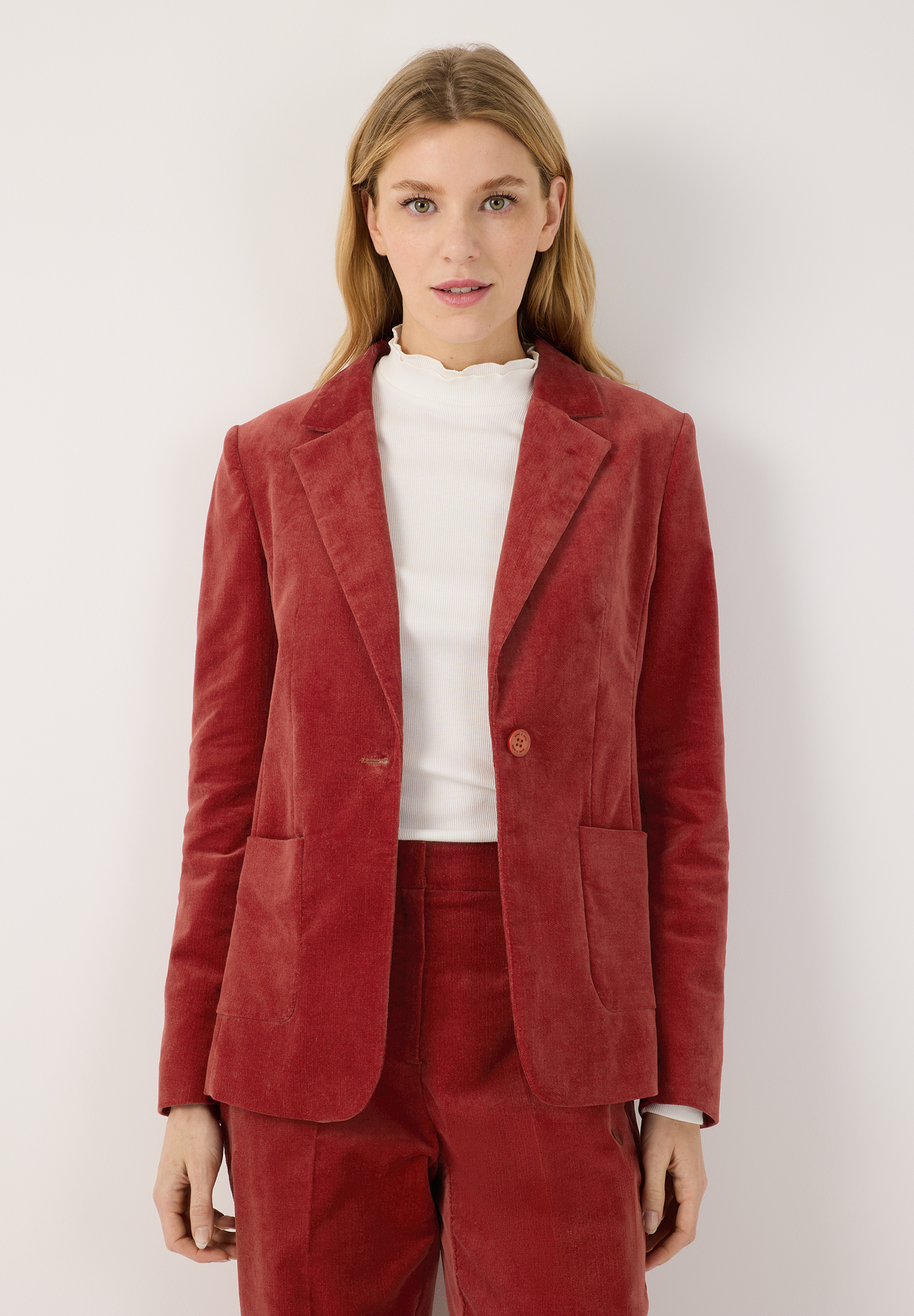 MORE & MORE Blazer: Eine junge Frau trägt einen rostroten Kordblazer und eine passende Hose vor weißem Hintergrund.