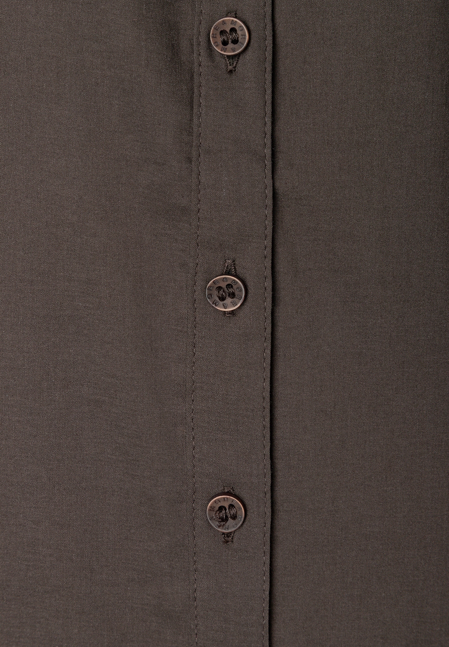MORE & MORE Bluse: Nahaufnahme der Knopfleiste eines dunkelbraunen MORE & MORE Oberteils mit drei Knöpfen. MORE & MORE Bluse: Nahaufnahme der Knopfleiste eines dunkelbraunen MORE & MORE Oberteils mit drei Knöpfen.