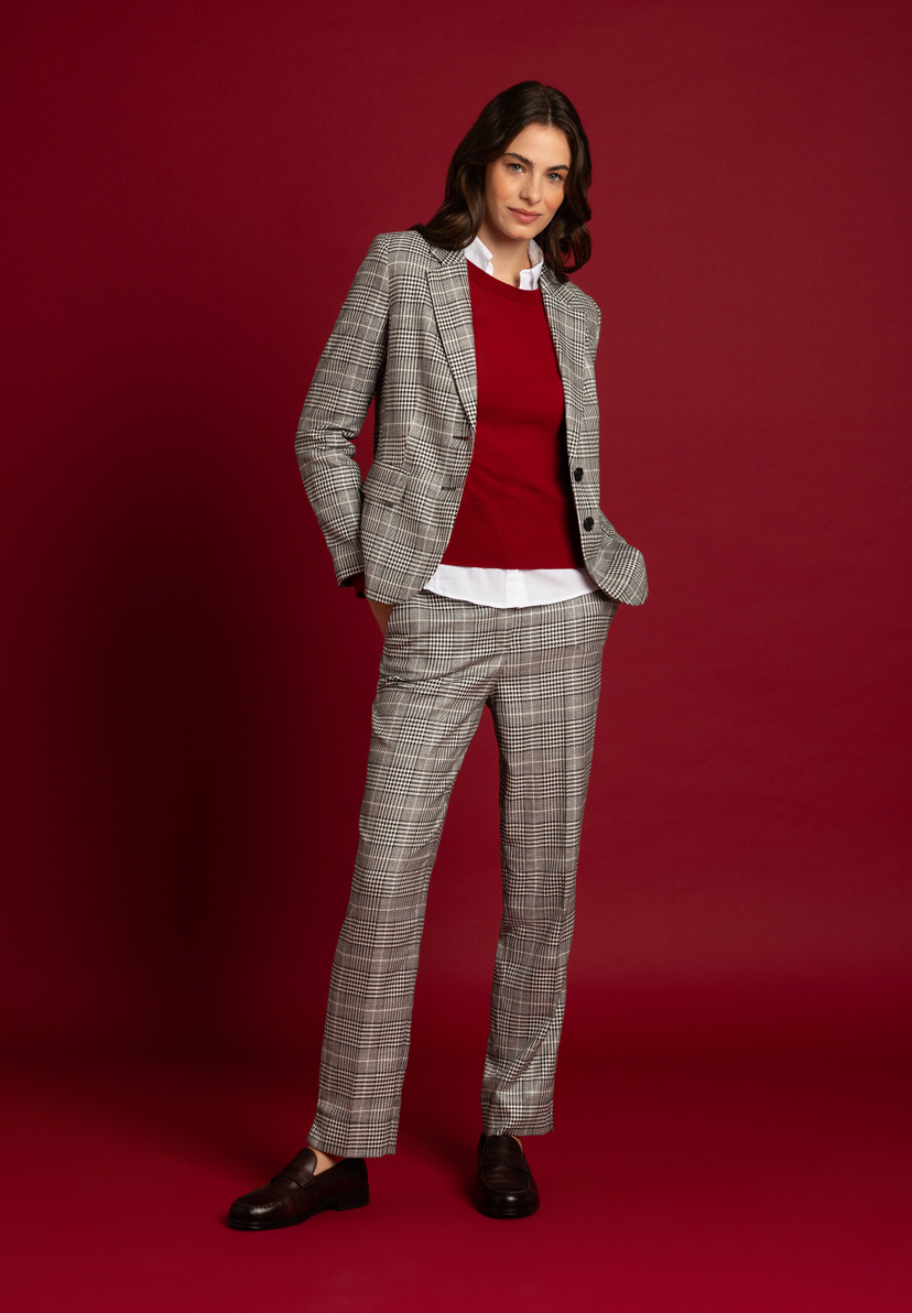 Eine Frau in MORE & MORE Hose und Blazer mit Karomuster vor weinrotem Hintergrund. Eine Frau in MORE & MORE Hose und Blazer mit Karomuster vor weinrotem Hintergrund.