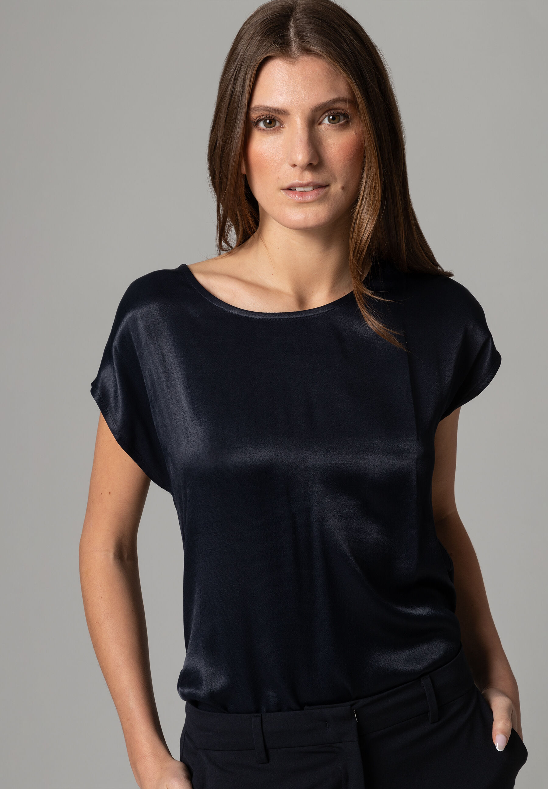 Eine Frau trägt ein schwarzes MORE & MORE Satin-Top. Schöner Glanz.