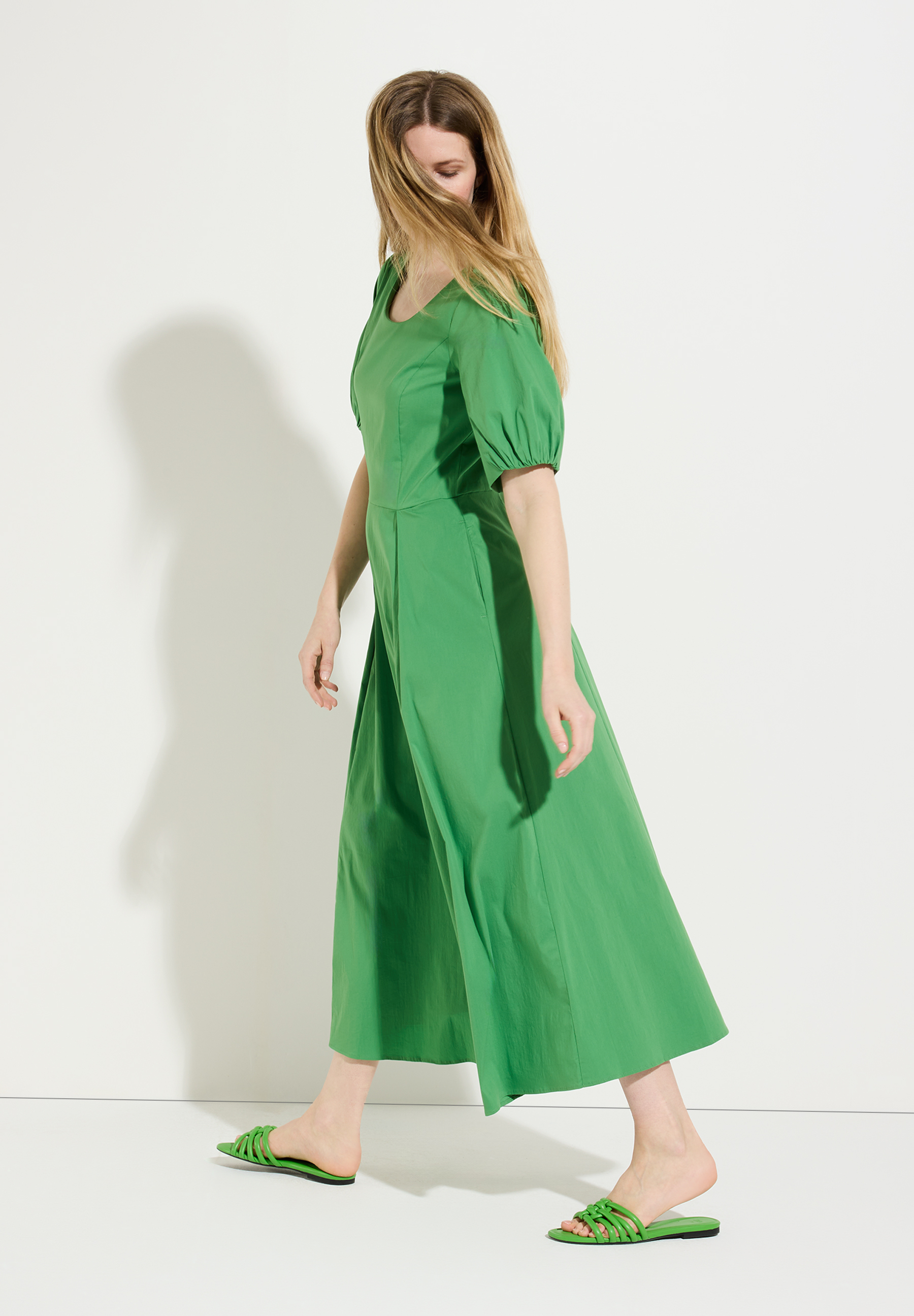 Eine Frau trägt ein grünes MORE & MORE Oberteil/Kleid aus Popeline mit Puffärmeln vor einer weißen Wand. Eine Frau trägt ein grünes MORE & MORE Oberteil/Kleid aus Popeline mit Puffärmeln vor einer weißen Wand.