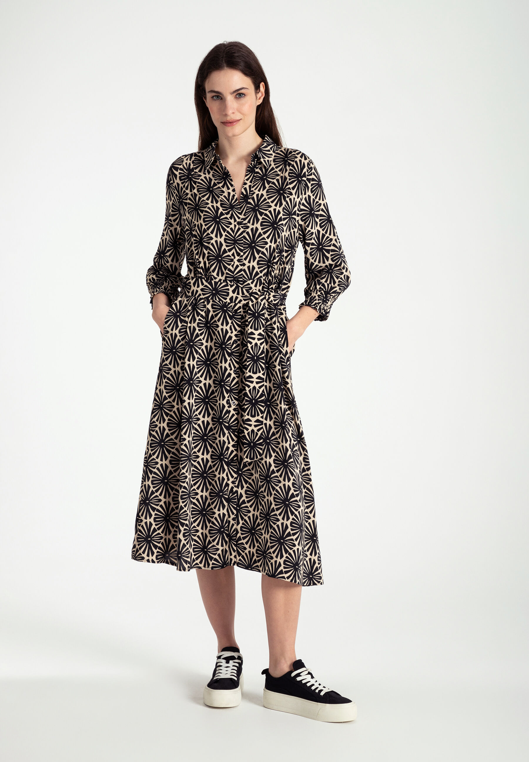 Eine Frau trägt ein Kleid von MORE & MORE mit fließender Viskose-Konstruktion. Das Oberteil hat ein schwarzes Blumenmuster. Eine Frau trägt ein Kleid von MORE & MORE mit fließender Viskose-Konstruktion. Das Oberteil hat ein schwarzes Blumenmuster.