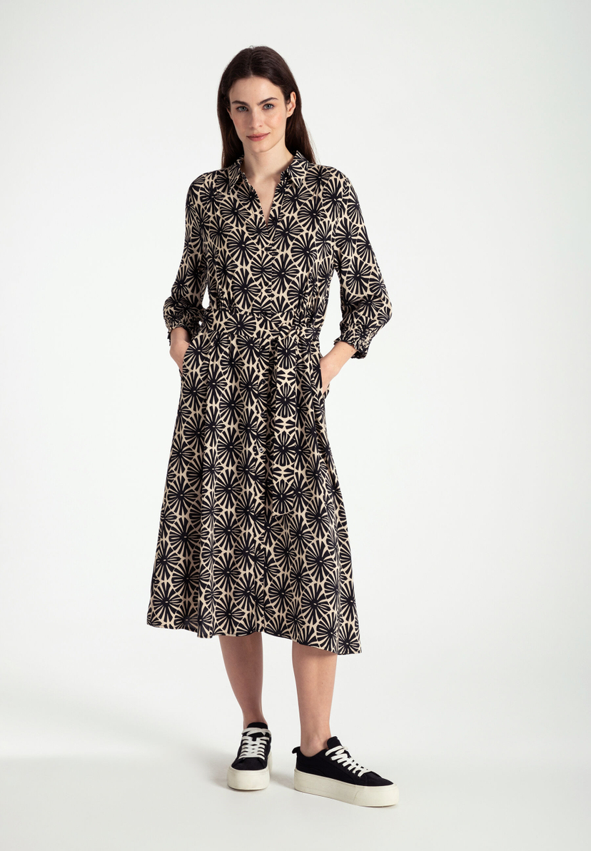 Eine Frau trägt ein Kleid von MORE & MORE mit fließender Viskose-Konstruktion. Das Oberteil hat ein schwarzes Blumenmuster. Eine Frau trägt ein Kleid von MORE & MORE mit fließender Viskose-Konstruktion. Das Oberteil hat ein schwarzes Blumenmuster.