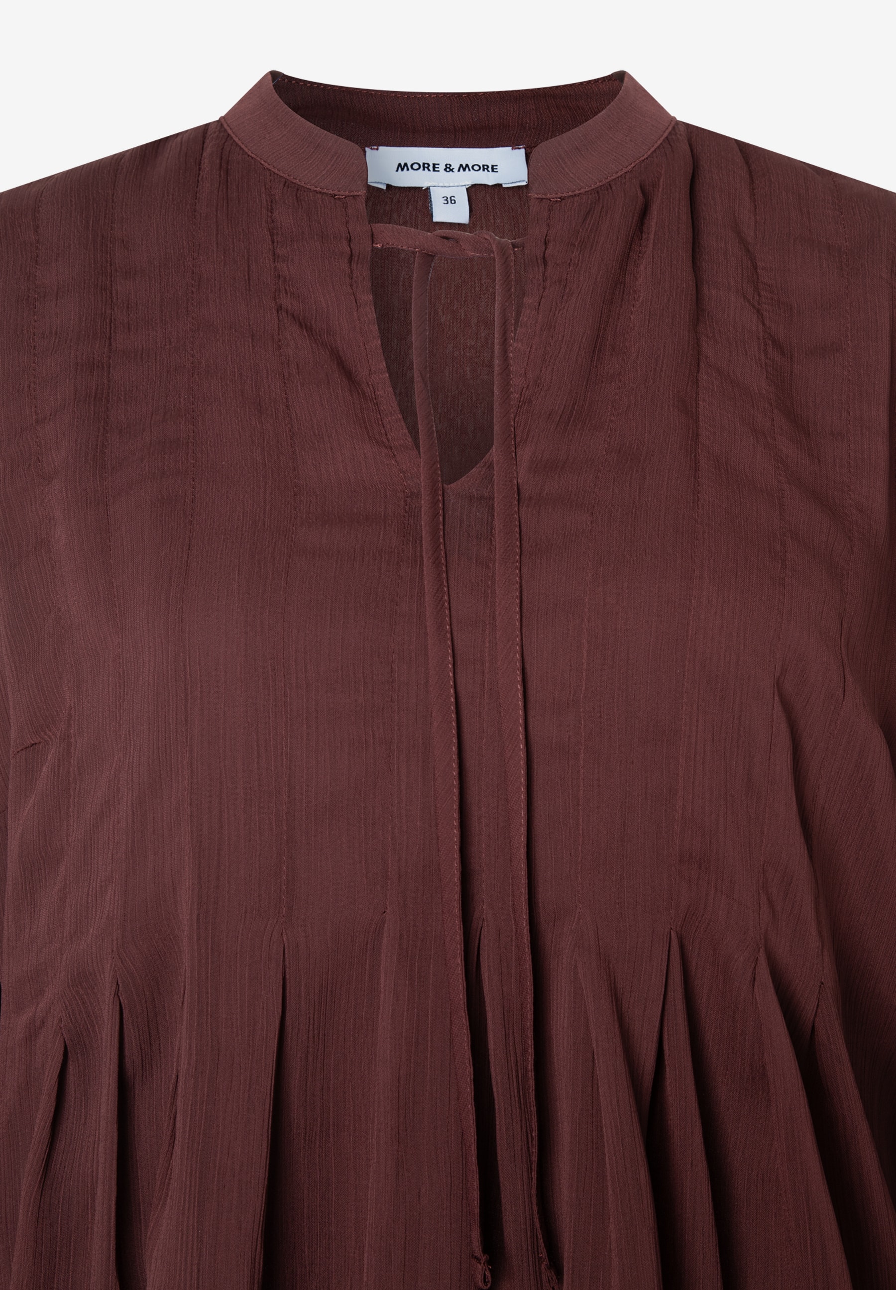 Nahaufnahme einer kastanienbraunen MORE & MORE Chiffon-Bluse mit Mandarinkragen und V-Ausschnitt mit Bindebändern. Nahaufnahme einer kastanienbraunen MORE & MORE Chiffon-Bluse mit Mandarinkragen und V-Ausschnitt mit Bindebändern.