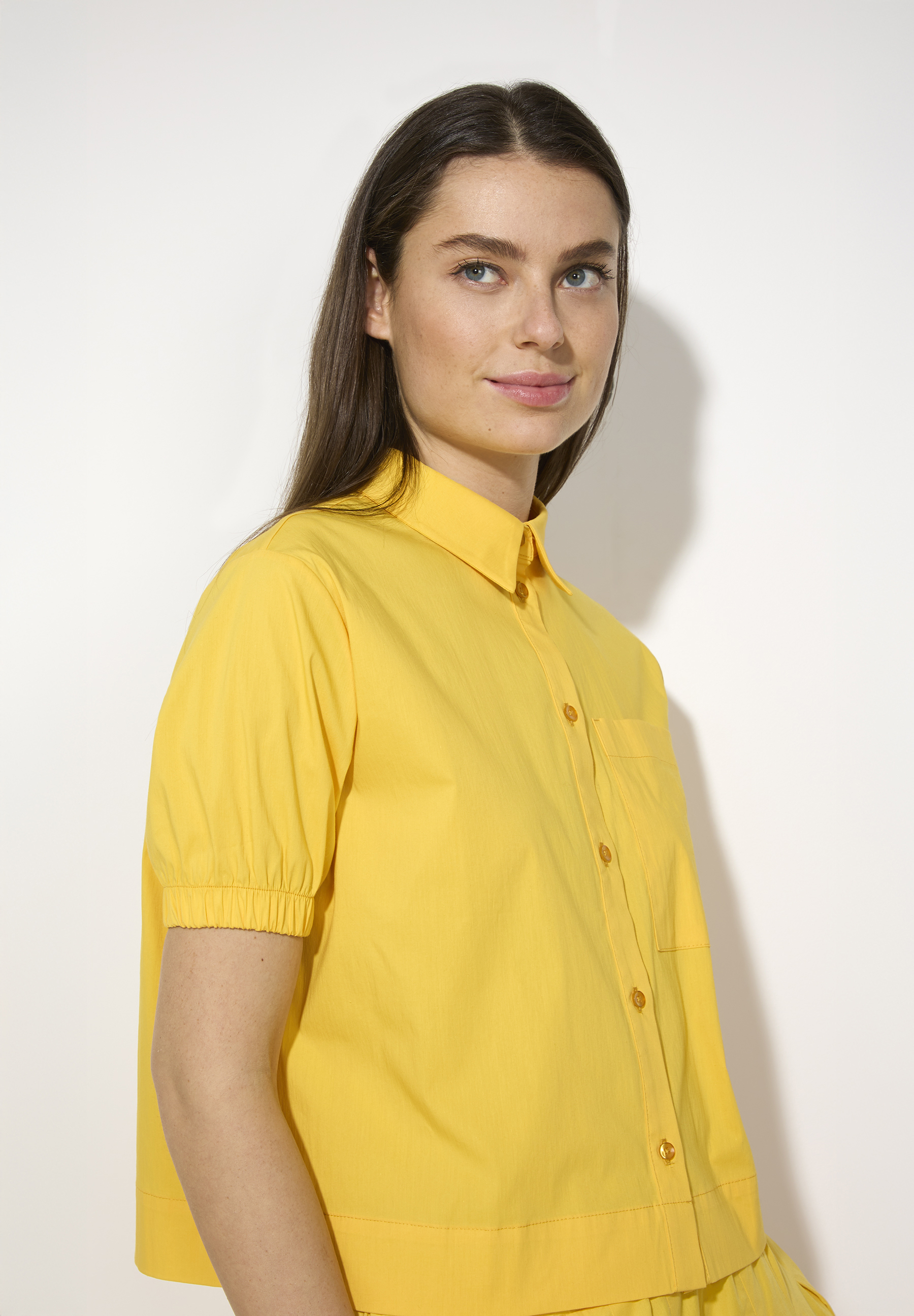Eine Frau trägt eine gelbe MORE & MORE Bluse aus Popeline mit kurzem Ärmel und Knopfleiste. Eine Frau trägt eine gelbe MORE & MORE Bluse aus Popeline mit kurzem Ärmel und Knopfleiste.