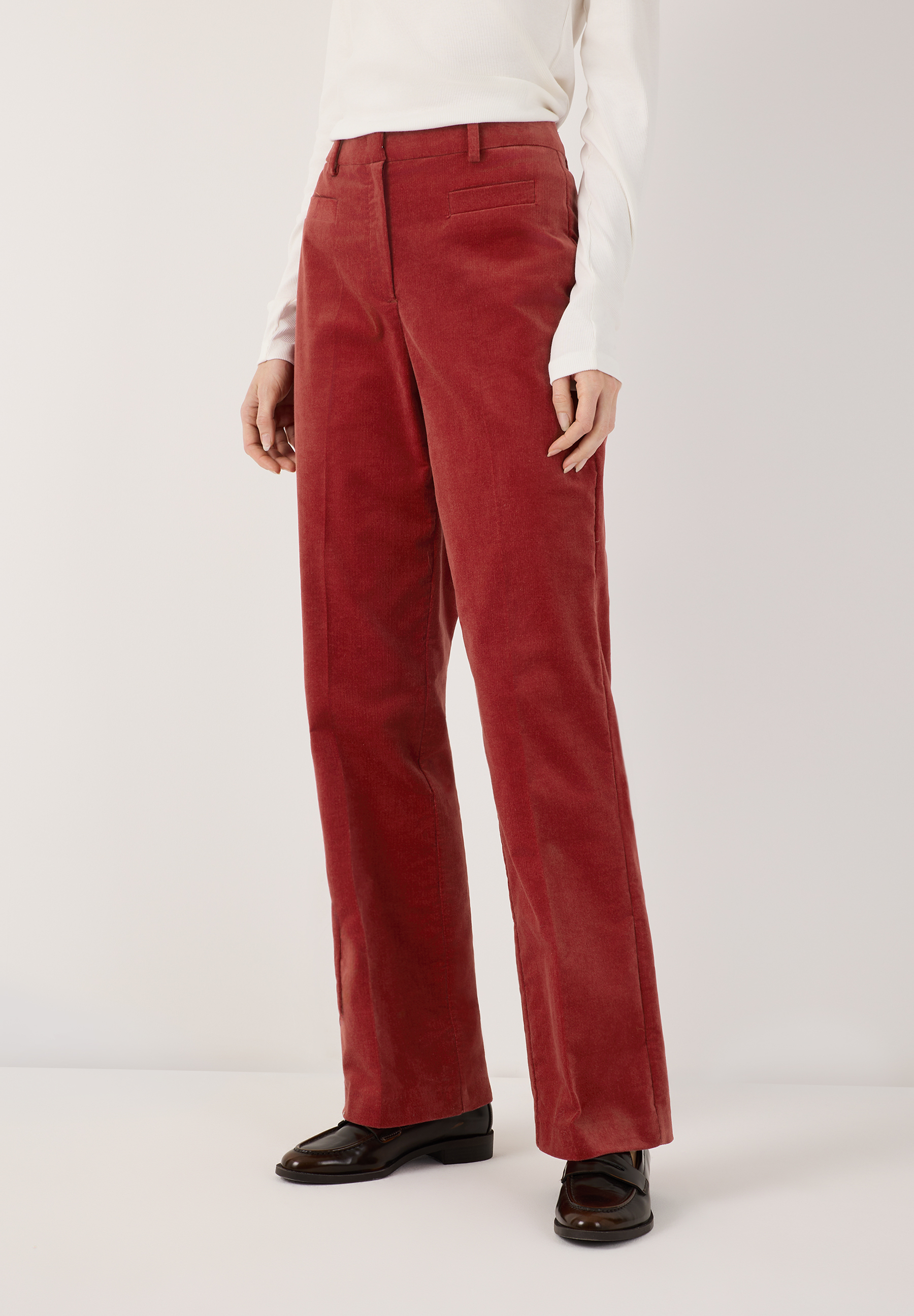 MORE & MORE Cordhose in Rostrot, kombiniert mit einem weißen Langarmshirt und dunklen Loafers, auf hellem Hintergrund.