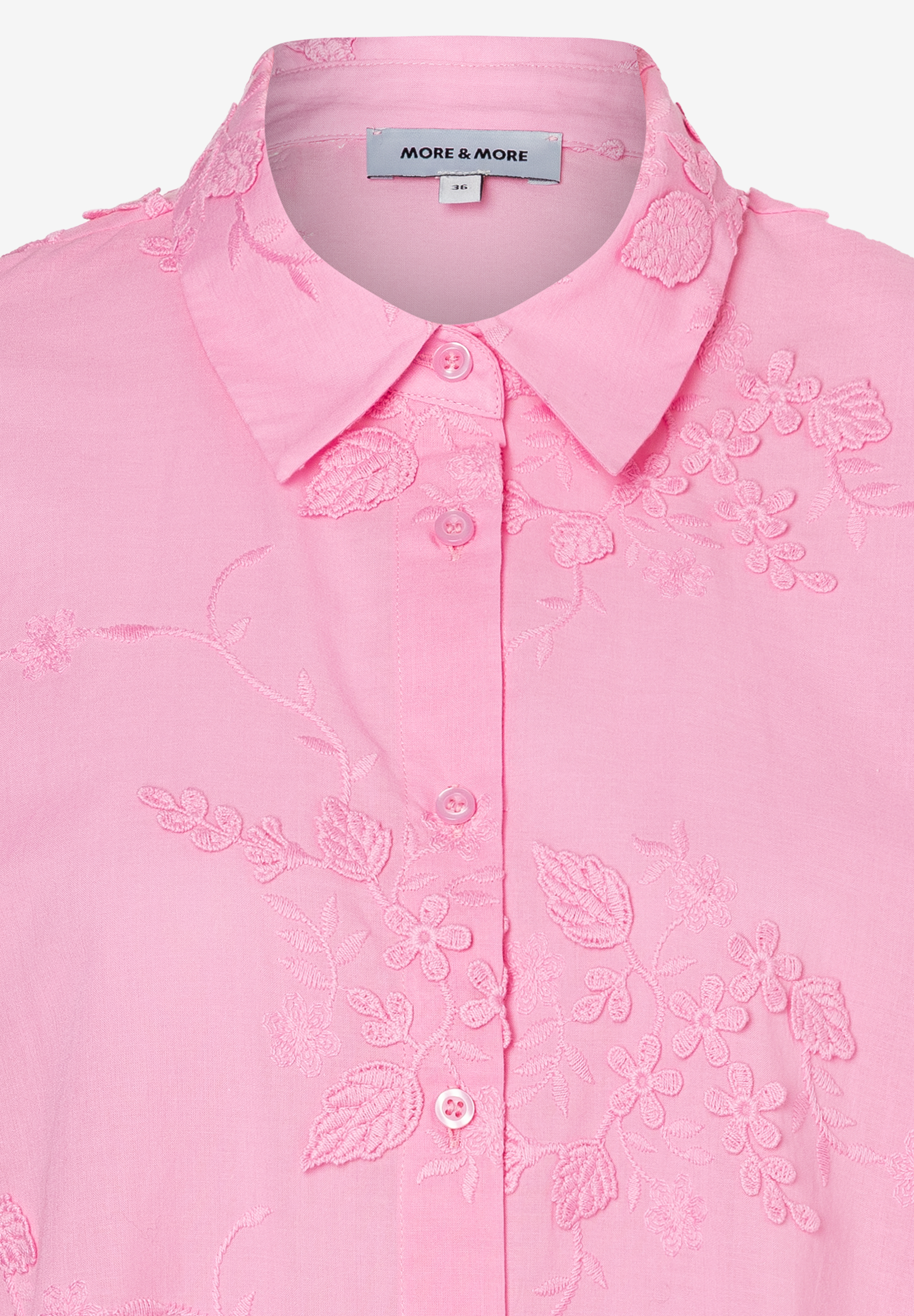 Nahaufnahme einer rosa MORE & MORE Bluse mit Blumenstickereien an Kragen und Knopfleiste. Nahaufnahme einer rosa MORE & MORE Bluse mit Blumenstickereien an Kragen und Knopfleiste.
