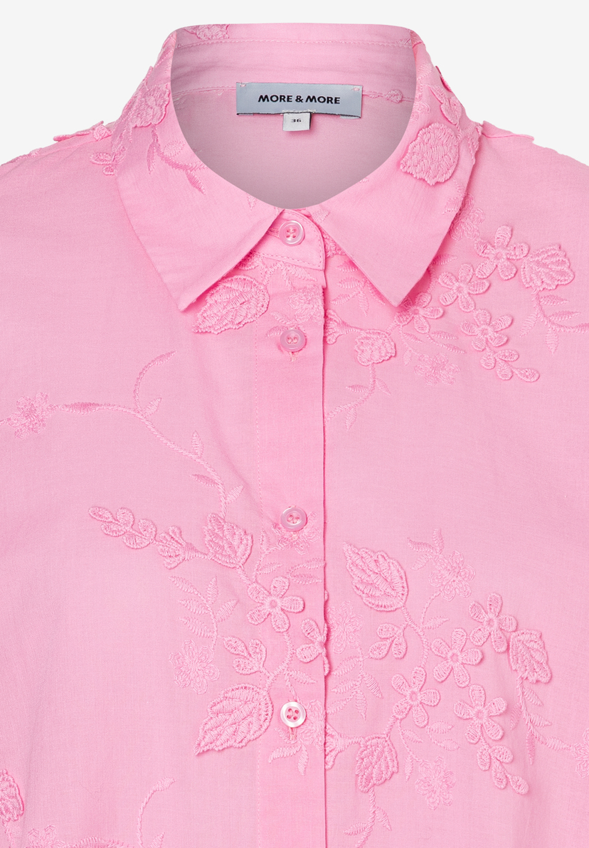 Nahaufnahme einer rosa MORE & MORE Bluse mit Blumenstickereien an Kragen und Knopfleiste. Nahaufnahme einer rosa MORE & MORE Bluse mit Blumenstickereien an Kragen und Knopfleiste.