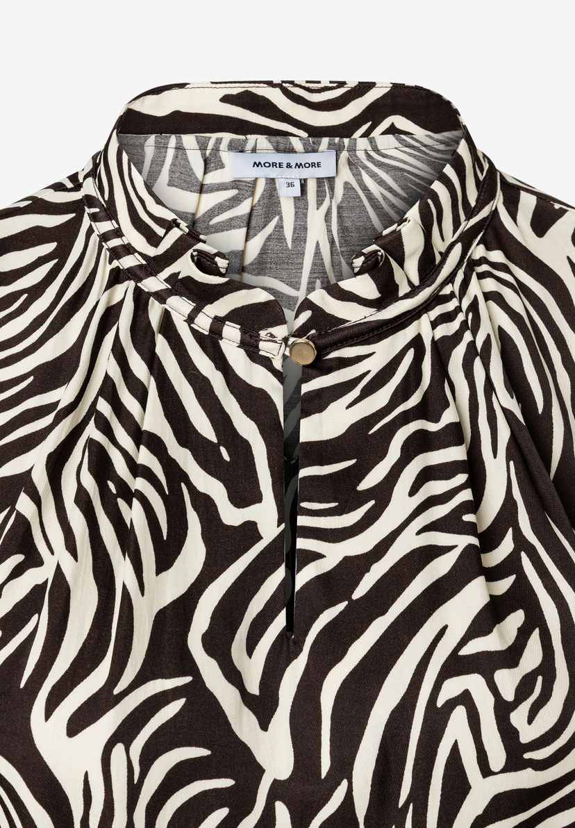 Nahaufnahme einer MORE & MORE Bluse mit Zebramuster aus fließender Viskose, Knopf am Kragen und Etikett. Nahaufnahme einer MORE & MORE Bluse mit Zebramuster aus fließender Viskose, Knopf am Kragen und Etikett.