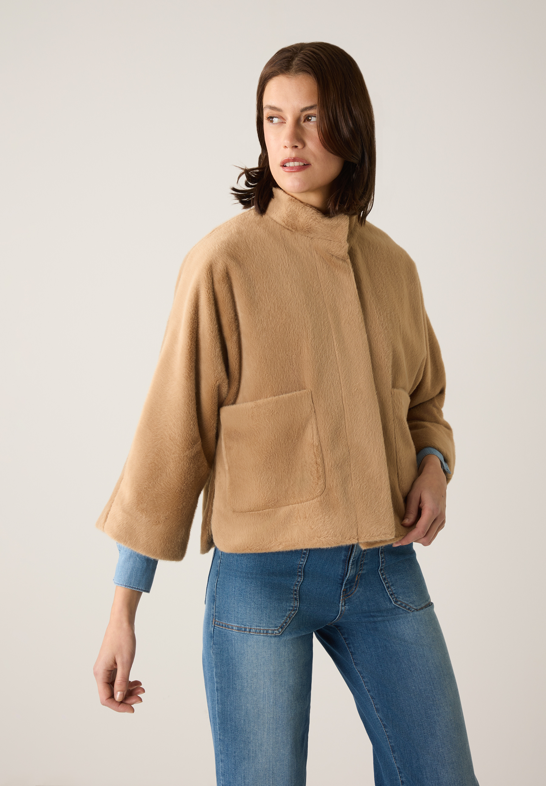 Eine Frau trägt eine hellbraune, wärmende MORE & MORE Jacke aus Kunstfell und blaue Jeans vor einem neutralen Hintergrund. Eine Frau trägt eine hellbraune, wärmende MORE & MORE Jacke aus Kunstfell und blaue Jeans vor einem neutralen Hintergrund.
